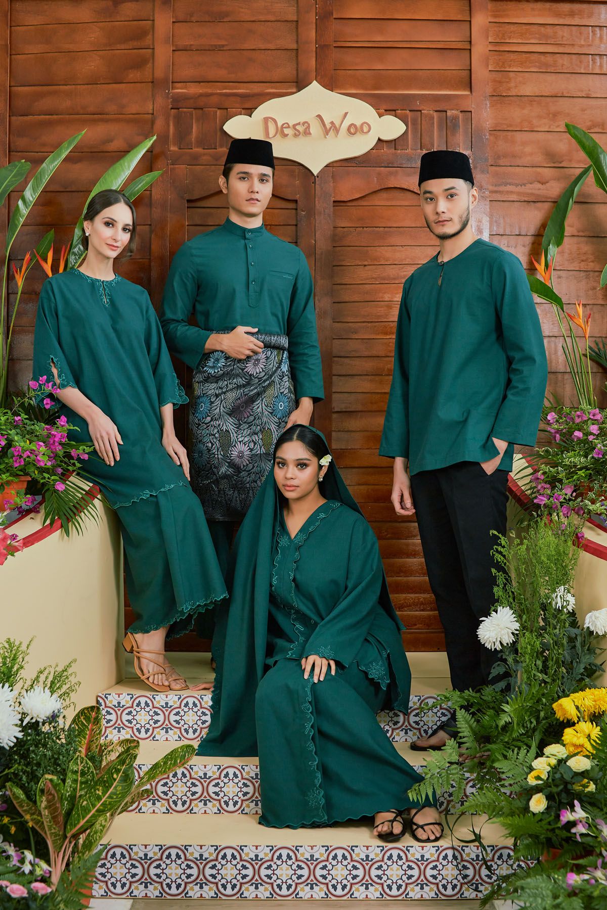 Four models in matching teal green baju kurung and baju melayu outfits posing at Desa Woo decorated entrance.