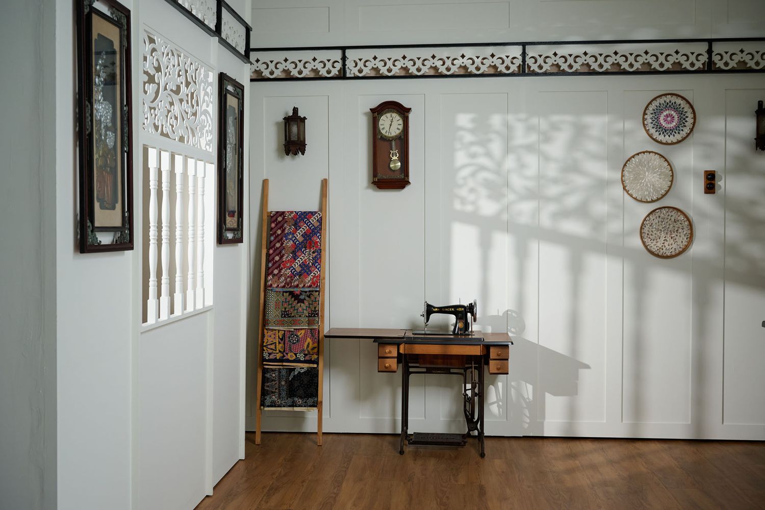 Vintage sewing room with antique sewing machine, wall clock, decorative baskets, and framed artwork on white walls.