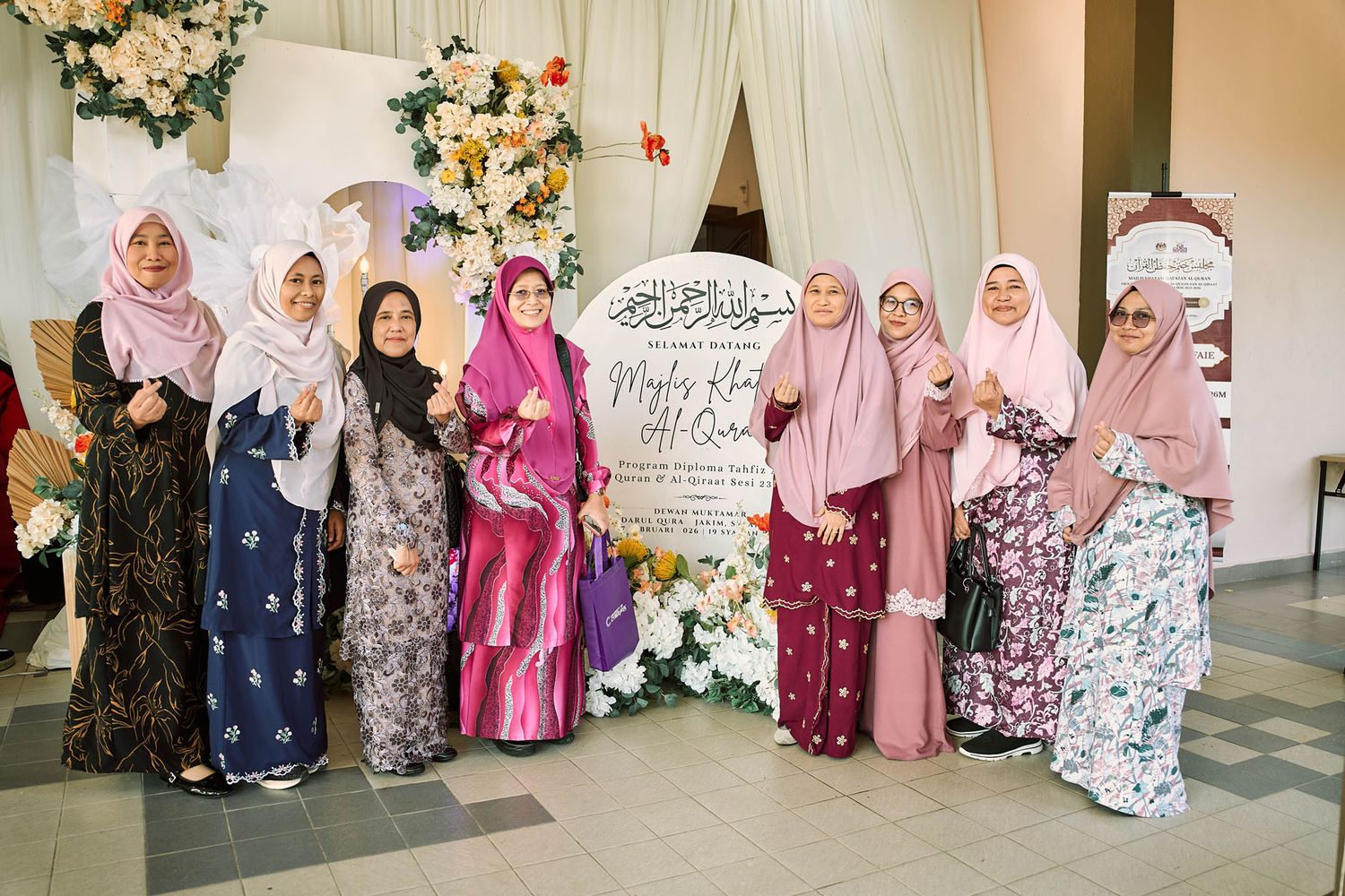 Group of women in colorful hijabs and baju kurung posing together at a decorated Islamic celebration event.
