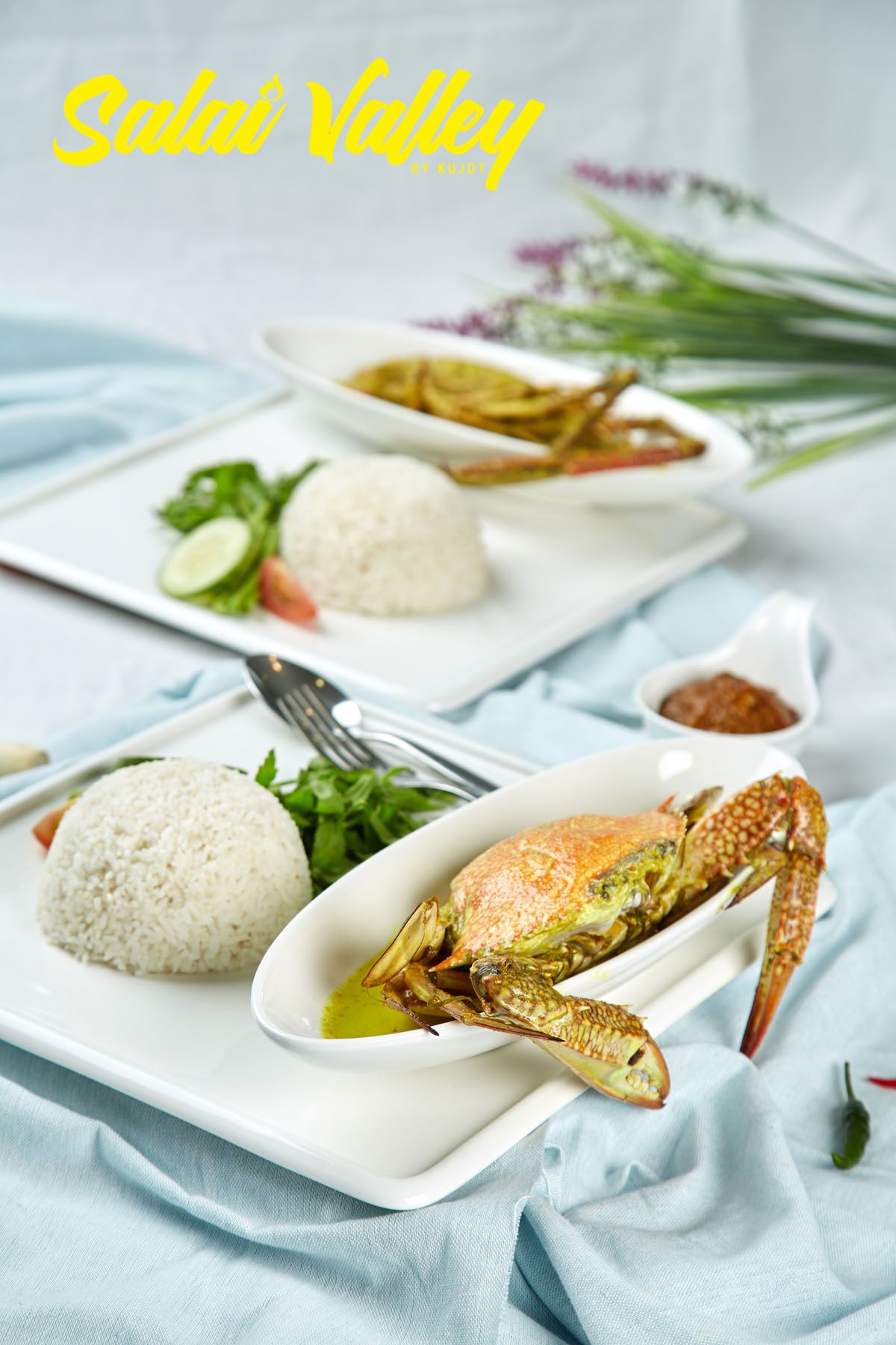 Two white plates of rice with green curry crab, sambal sauce, and fresh herbs from Sulai Valley.