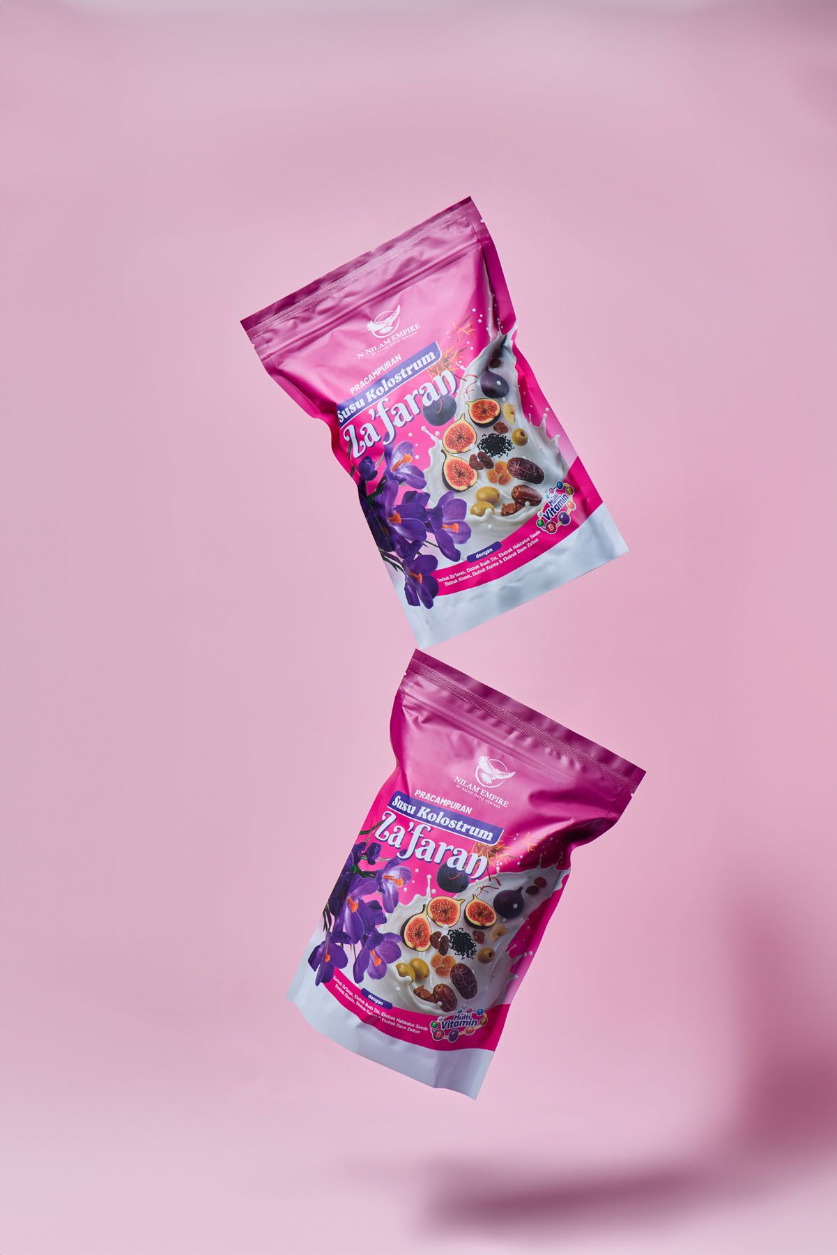 Two pink Za'faran Susu Kolostrum supplement pouches floating against a bright pink background.