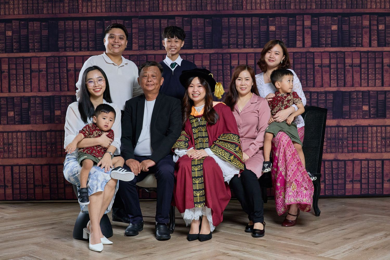 Asian family portrait with nine members including two toddlers posing in front of bookshelf background.