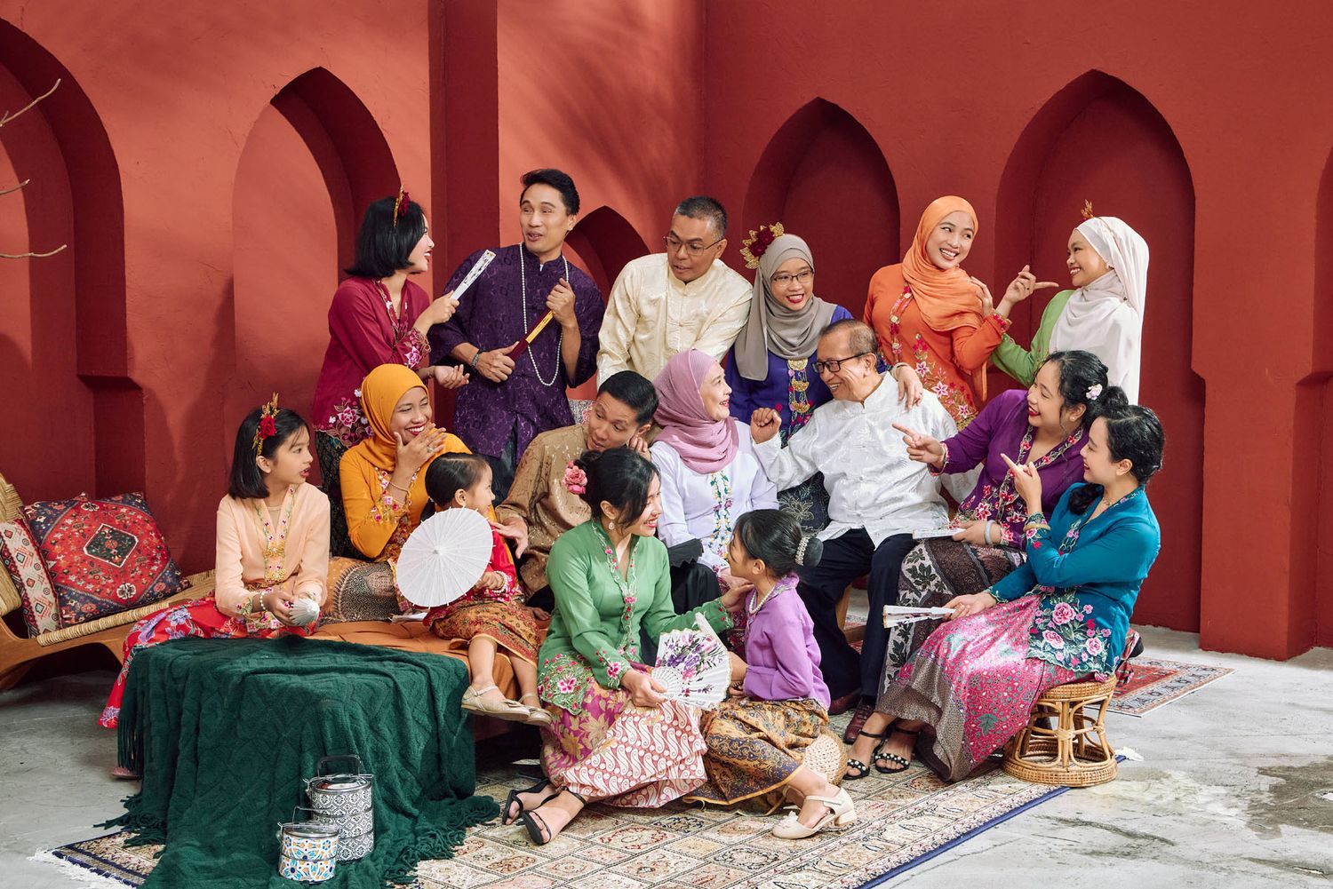 Large multigenerational Malaysian family in colorful traditional Malay attire gathered for festive Eid celebration.