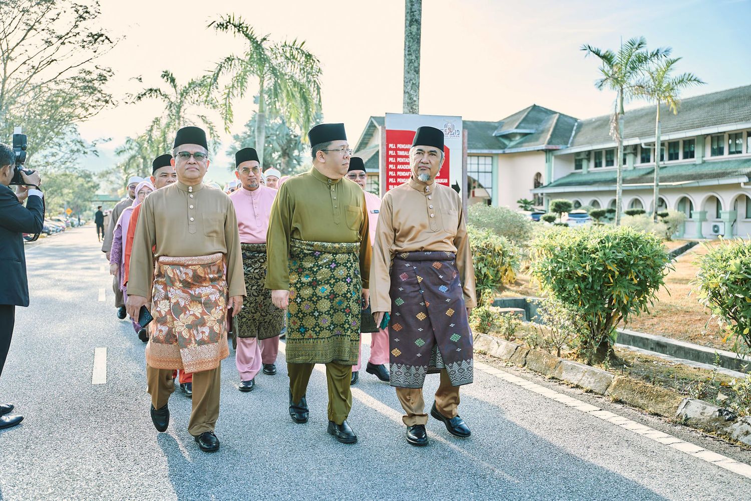Men in traditional Malaysian Baju Melayu attire walking along a road during a formal cultural procession.