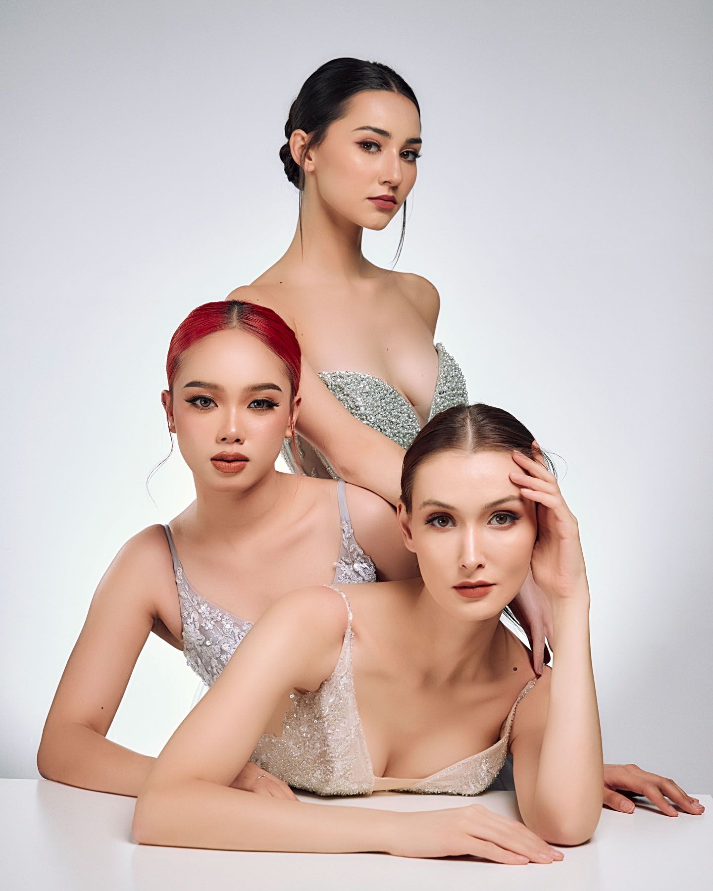 Three women in sparkly embellished tops posing together against a white studio background.