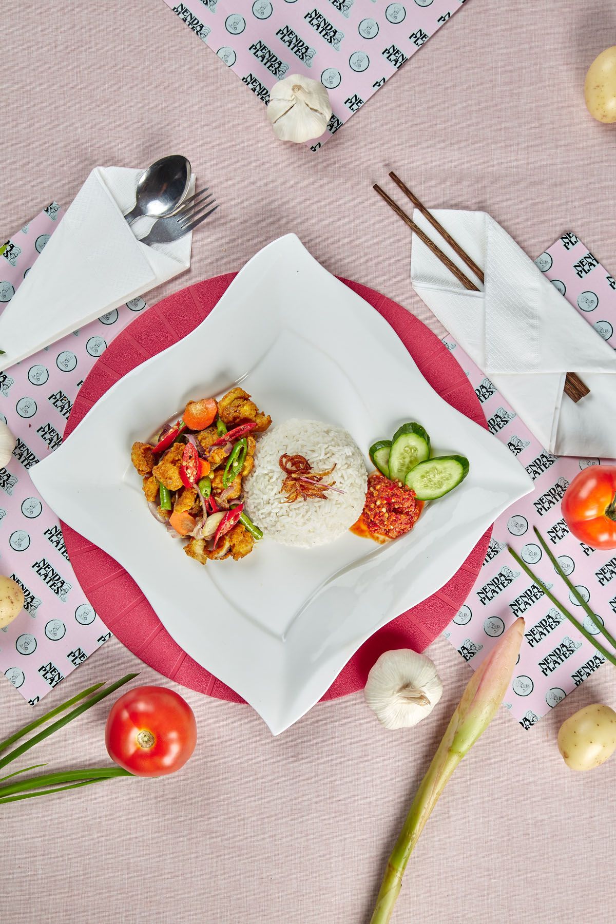 Asian rice dish with stir-fried vegetables, sambal, and cucumber slices on white square plate with chopsticks.