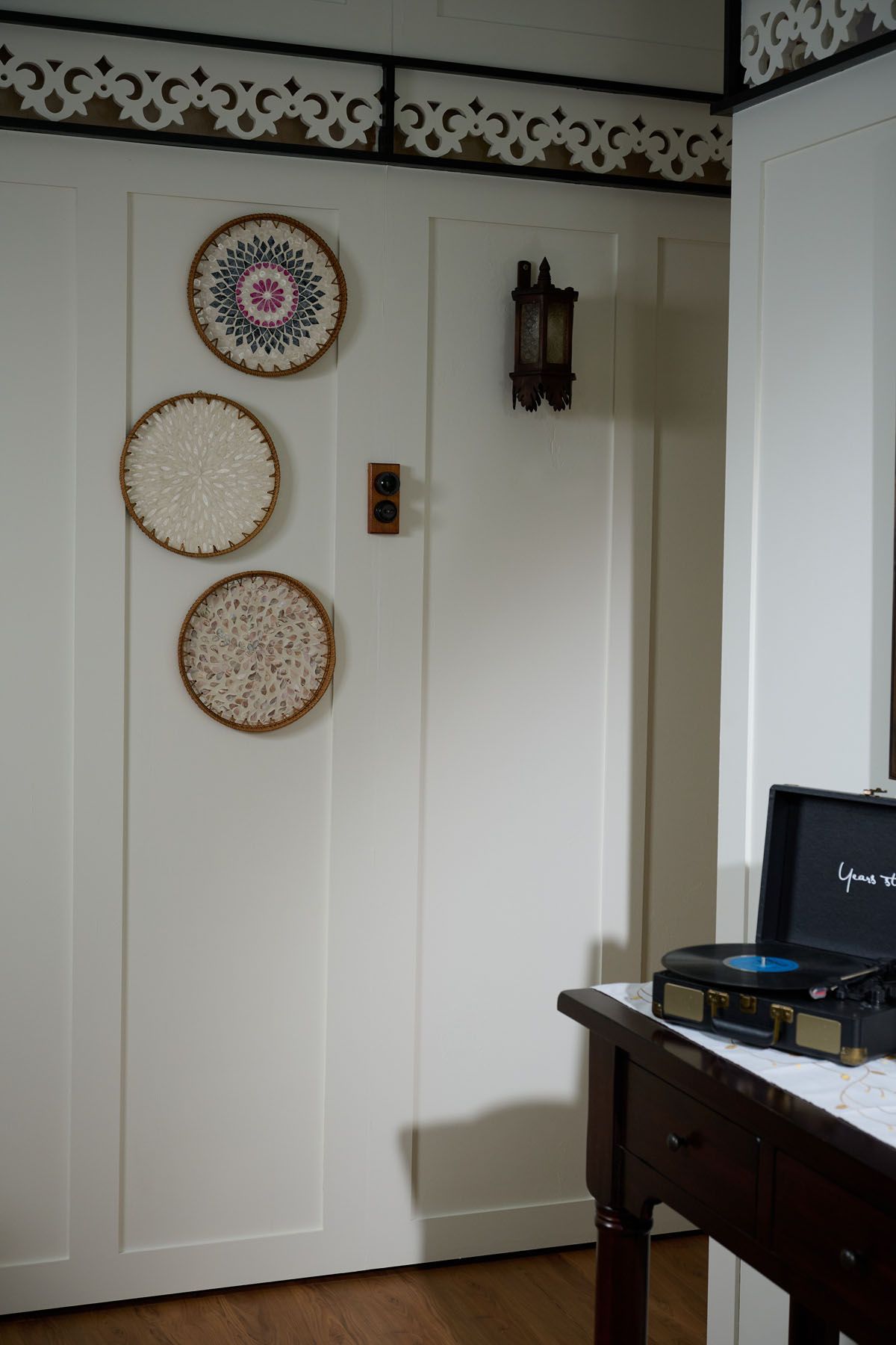 Vintage room with decorative woven wall plates, antique sconce, and a retro record player on a dark wood side table.