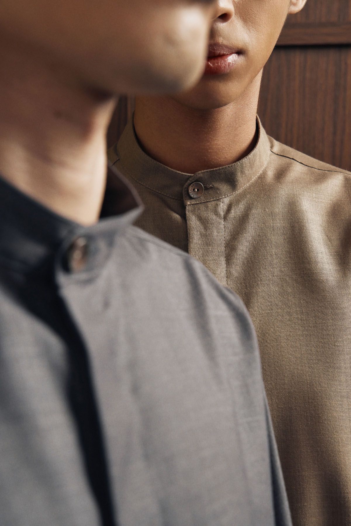 Close-up of two men wearing mandarin collar shirts in gray and tan with button details.