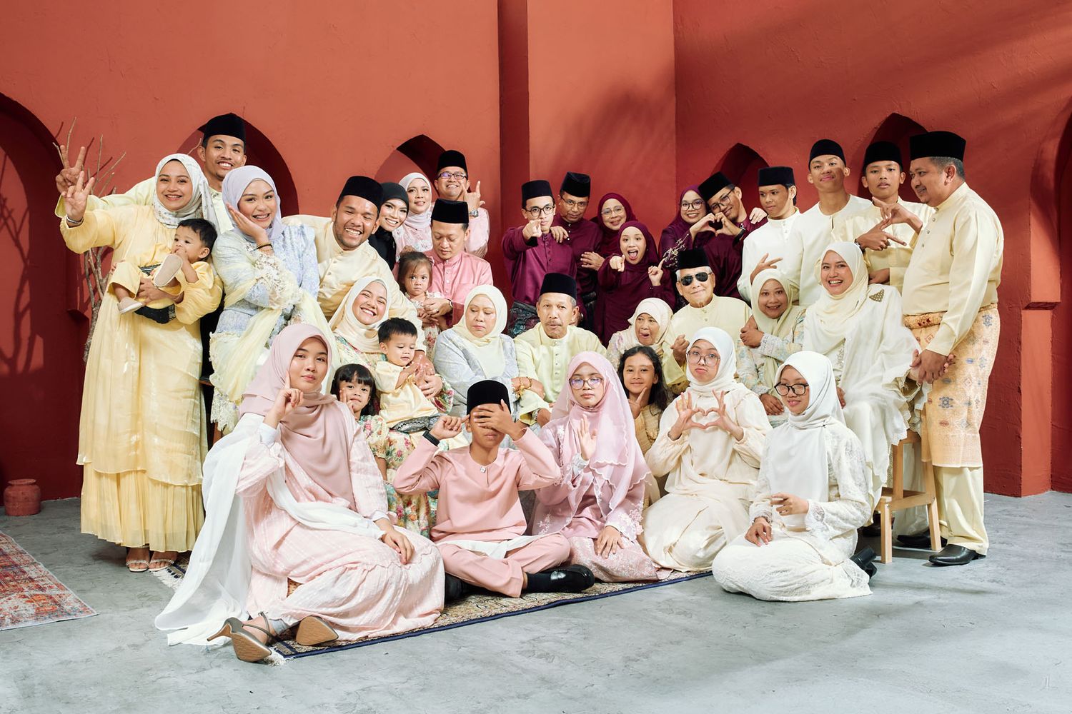 Extended Malaysian family dressed in coordinating white and pink traditional Raya attire group photo.