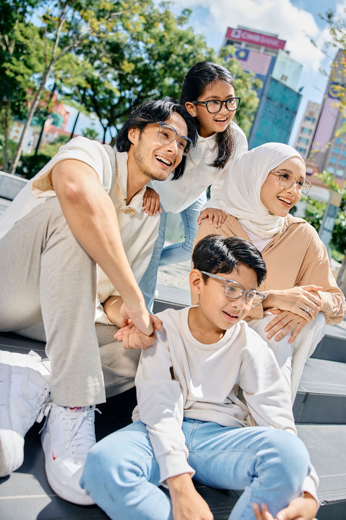 Happy family of four with two children smile together on outdoor steps on a sunny day.