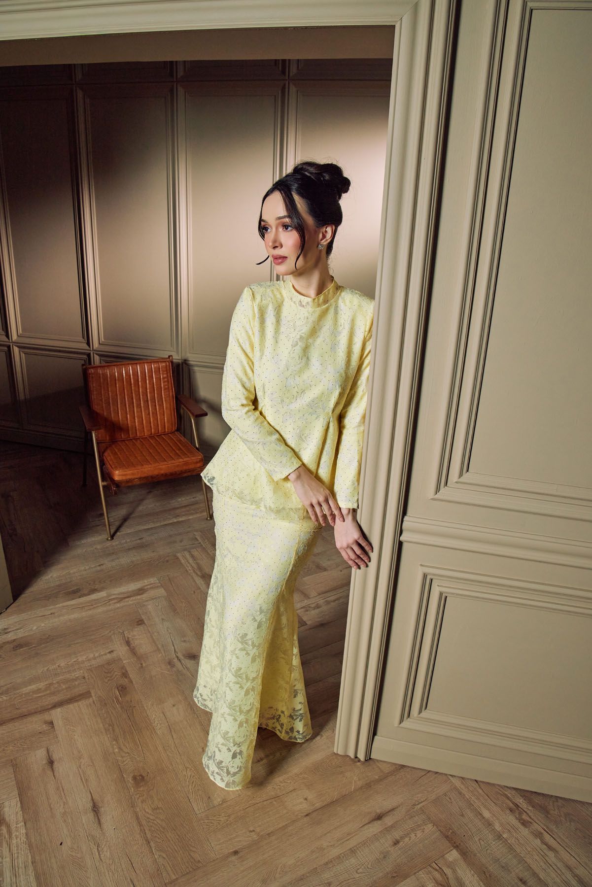Woman in yellow lace baju kurung set poses in elegant interior room.
