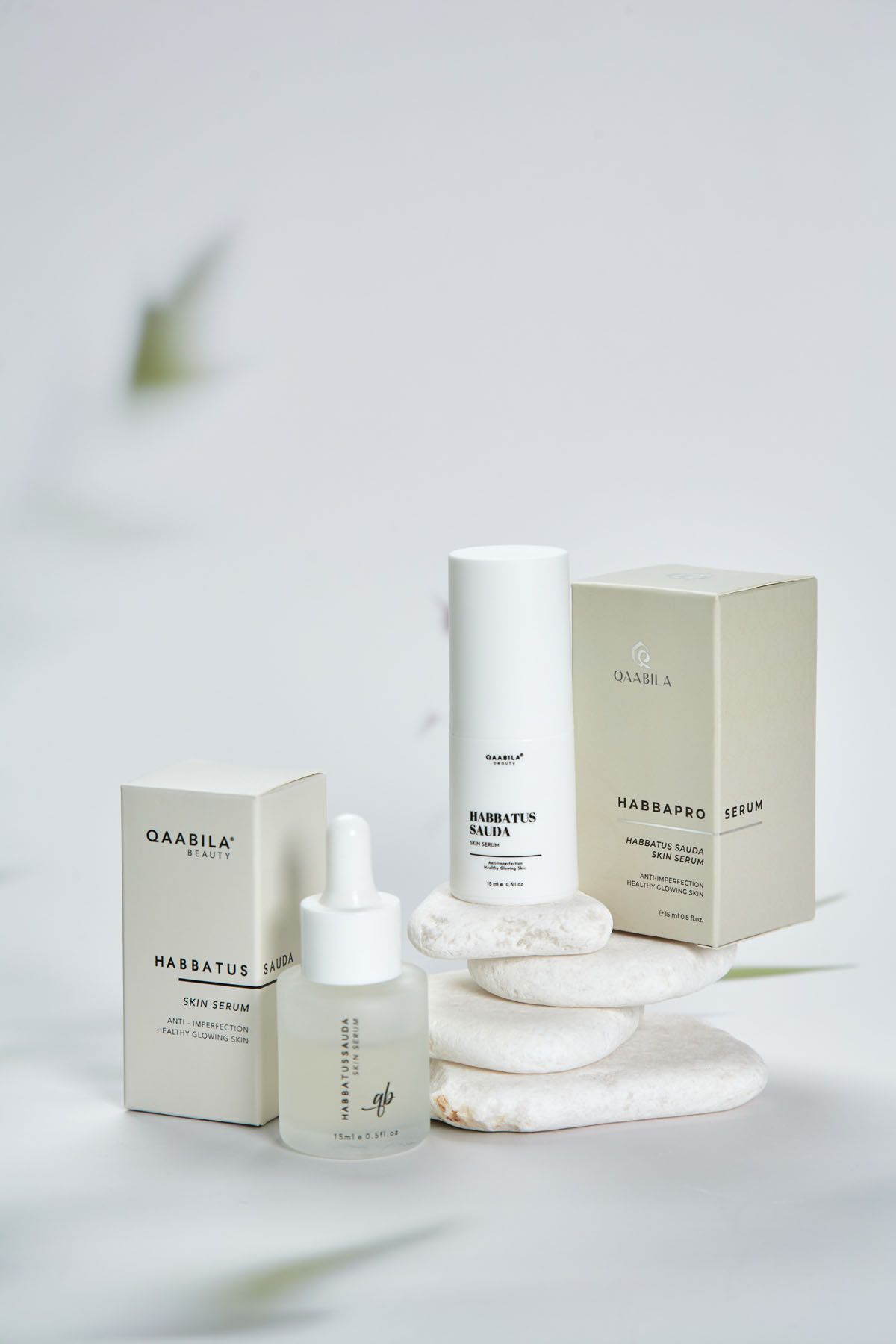 Qaabila beauty Habbatus Sauda skin serum with dropper bottle, pump bottle, and beige box on white stone pedestals.
