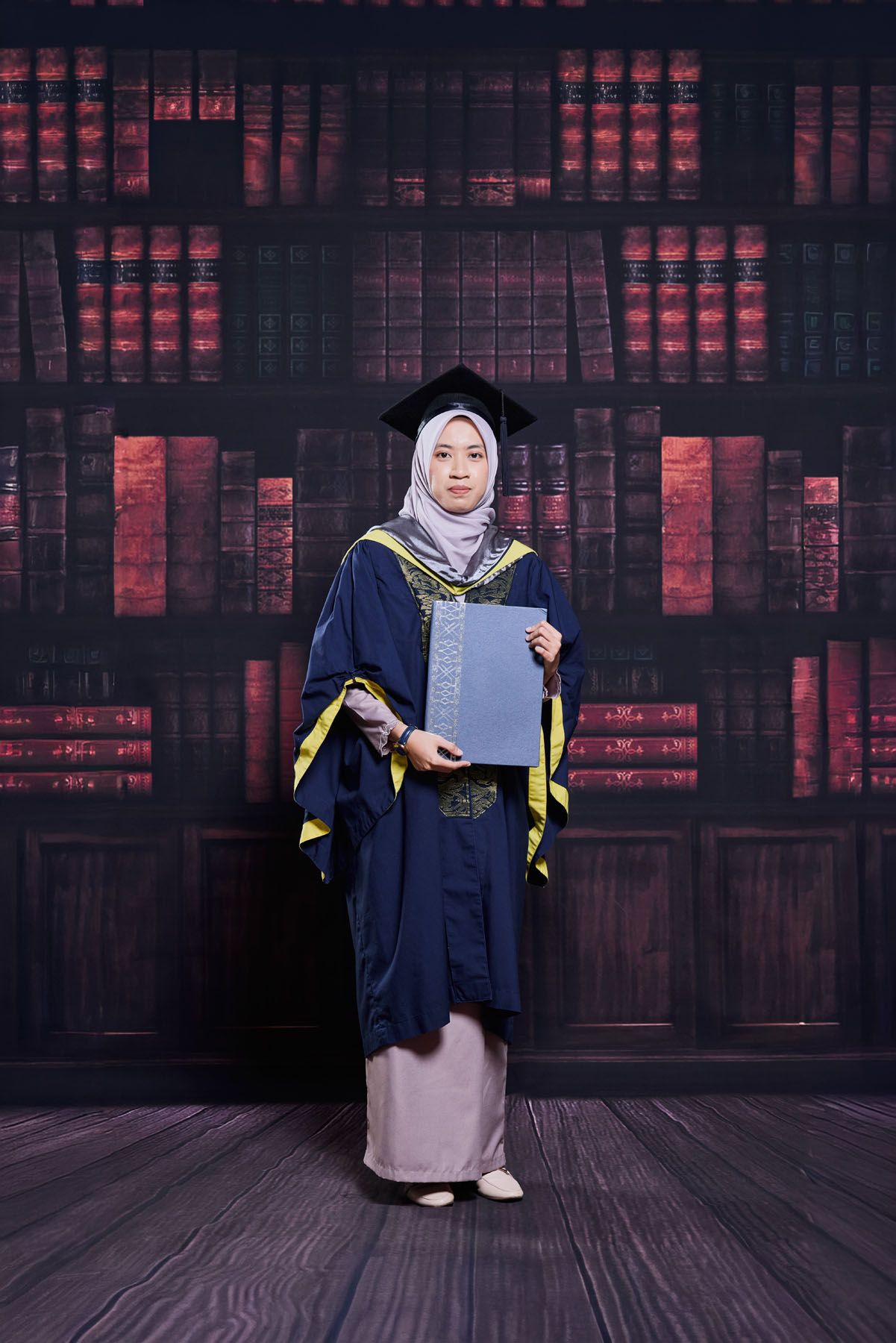 Muslim woman graduate in navy blue gown and hijab holding diploma at ceremony.