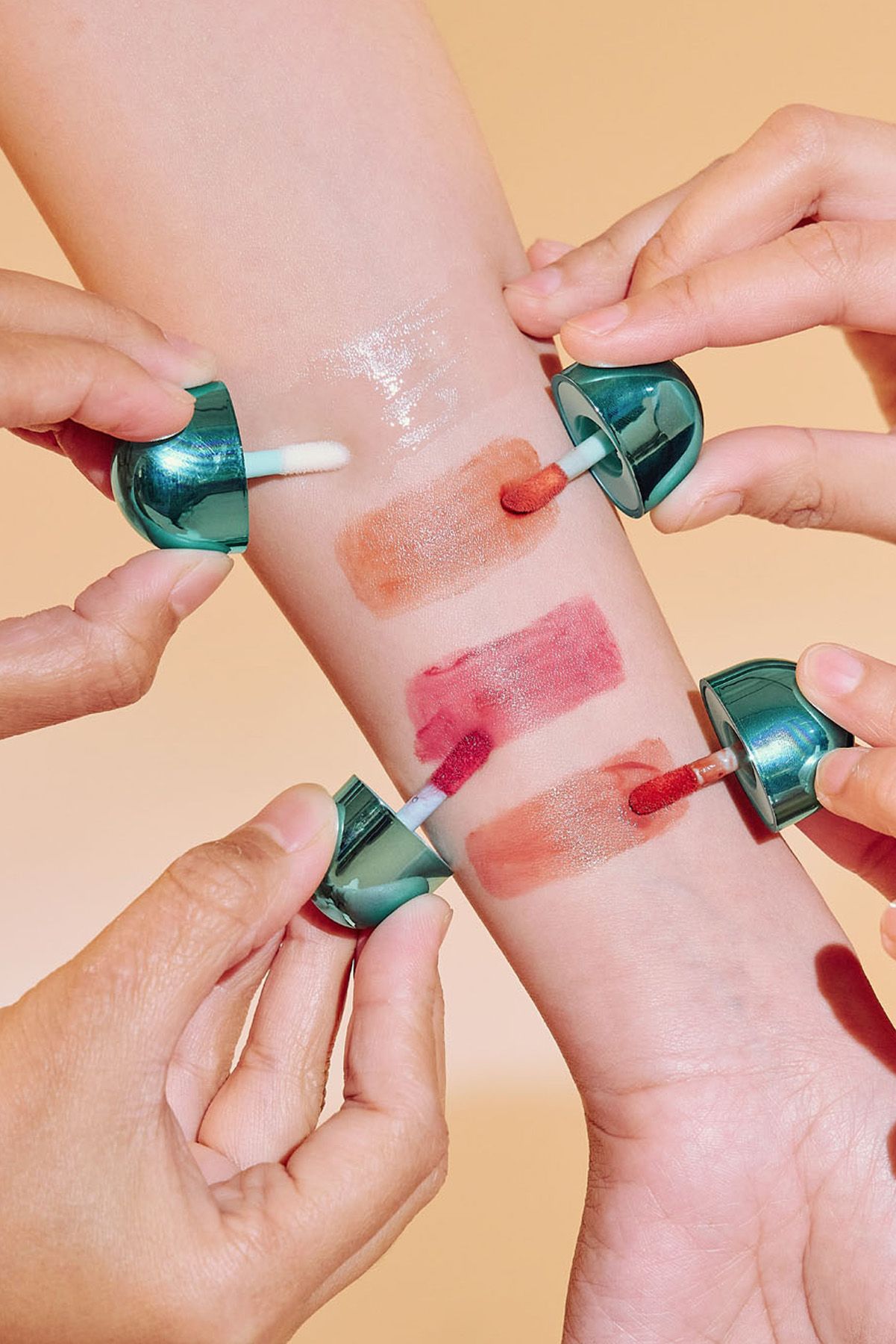 Multiple hands applying Ayla Cosmetics Twist lip gloss color swatches onto forearm skin.