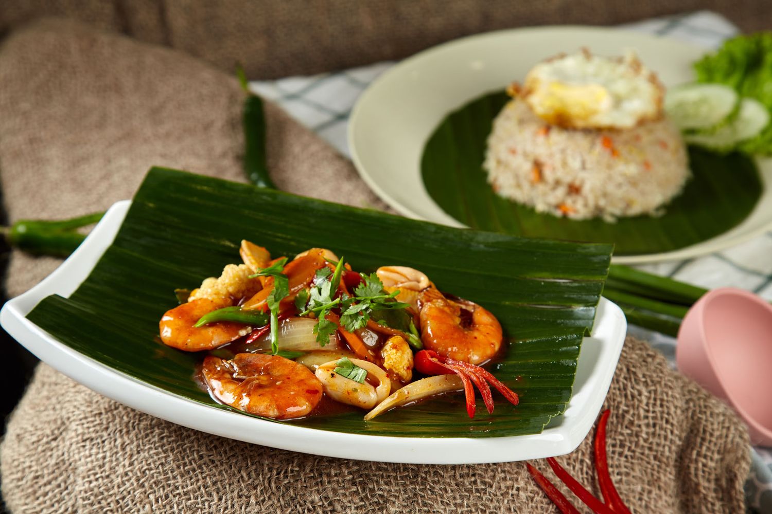 Stir-fried shrimp and squid in savory sauce served on banana leaf beside fried rice with egg.