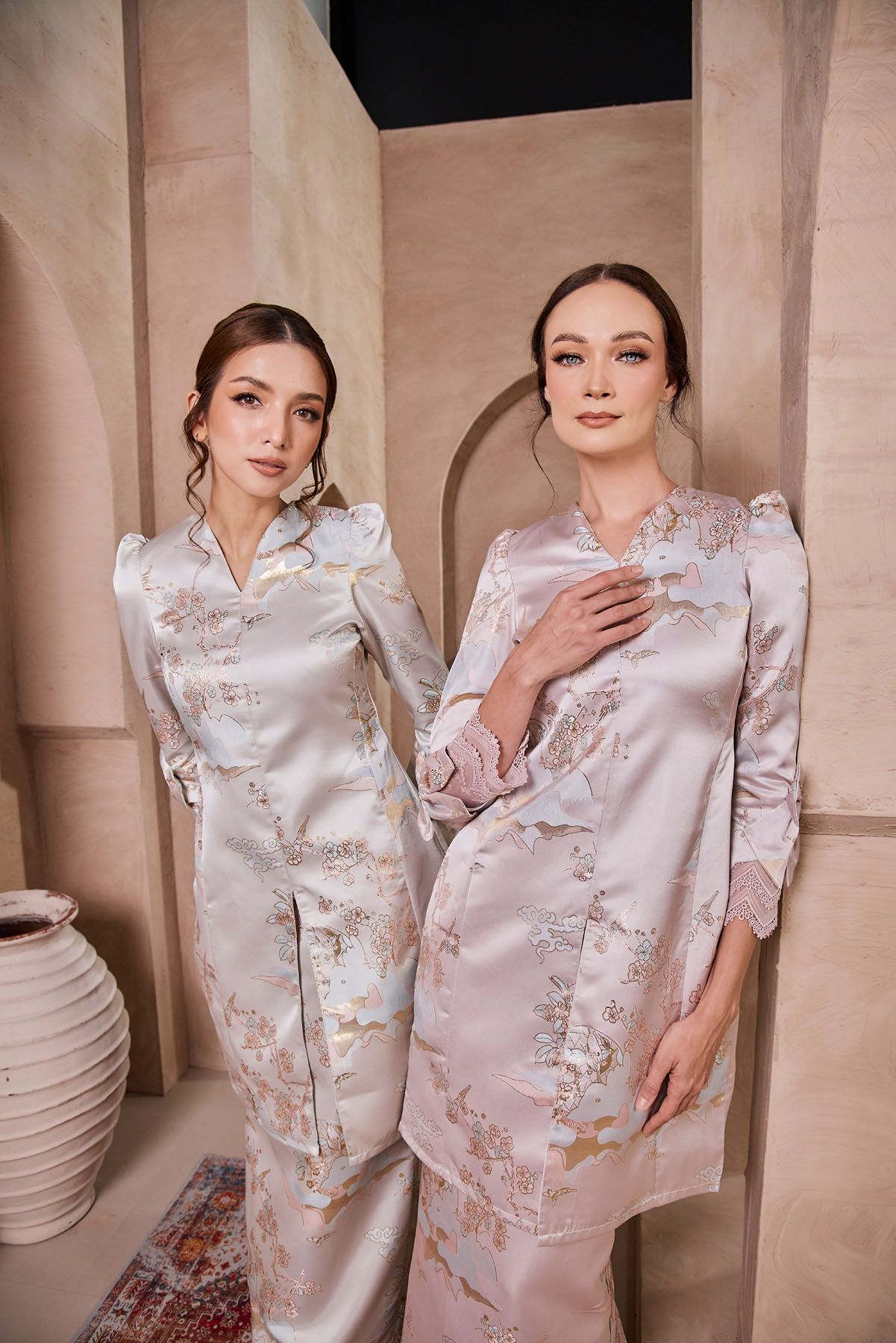 Two women in silver and pink floral brocade baju kurung modern pose together.