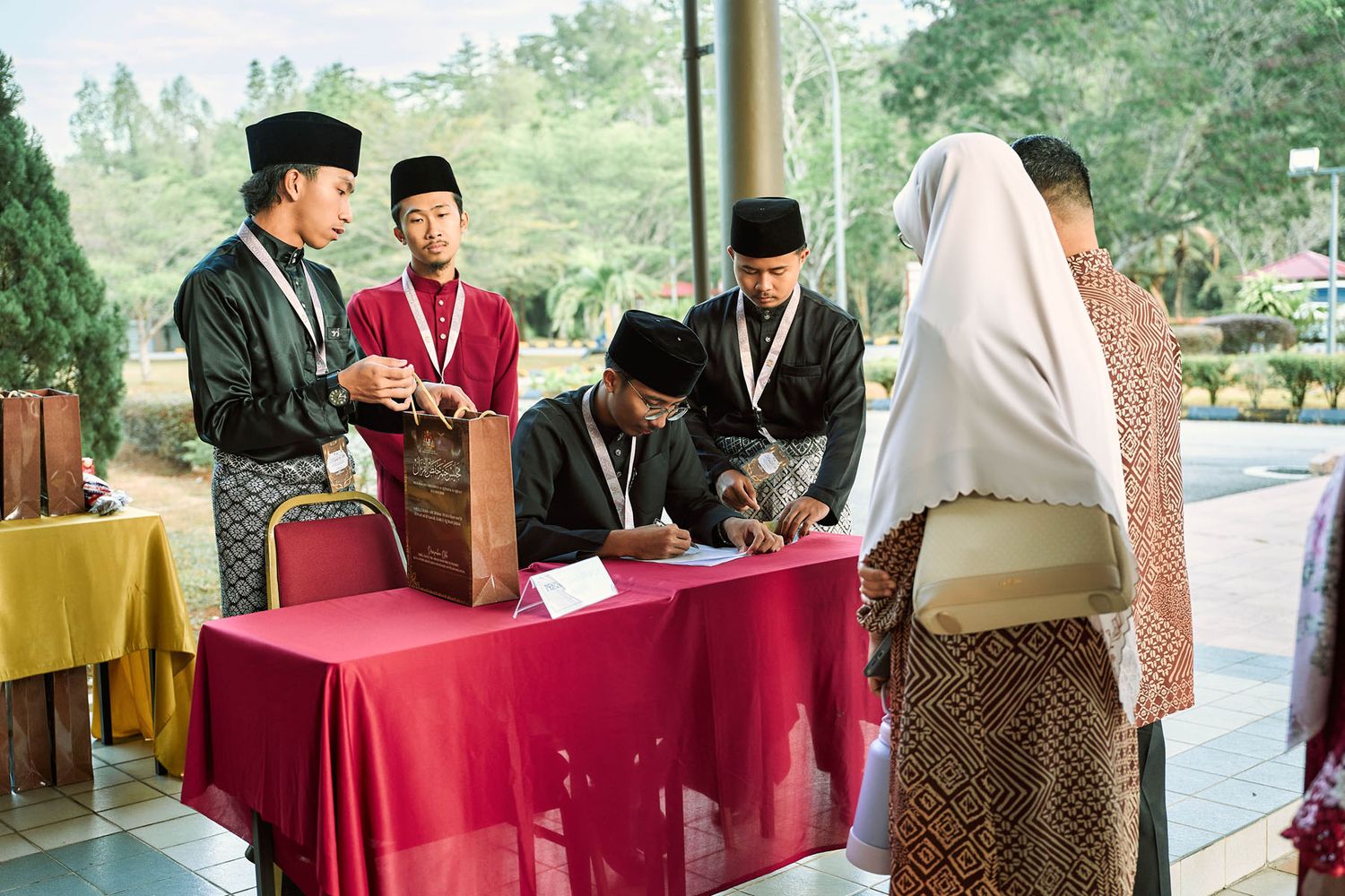 Men in traditional Malay attire managing registration table at formal Islamic ceremony.