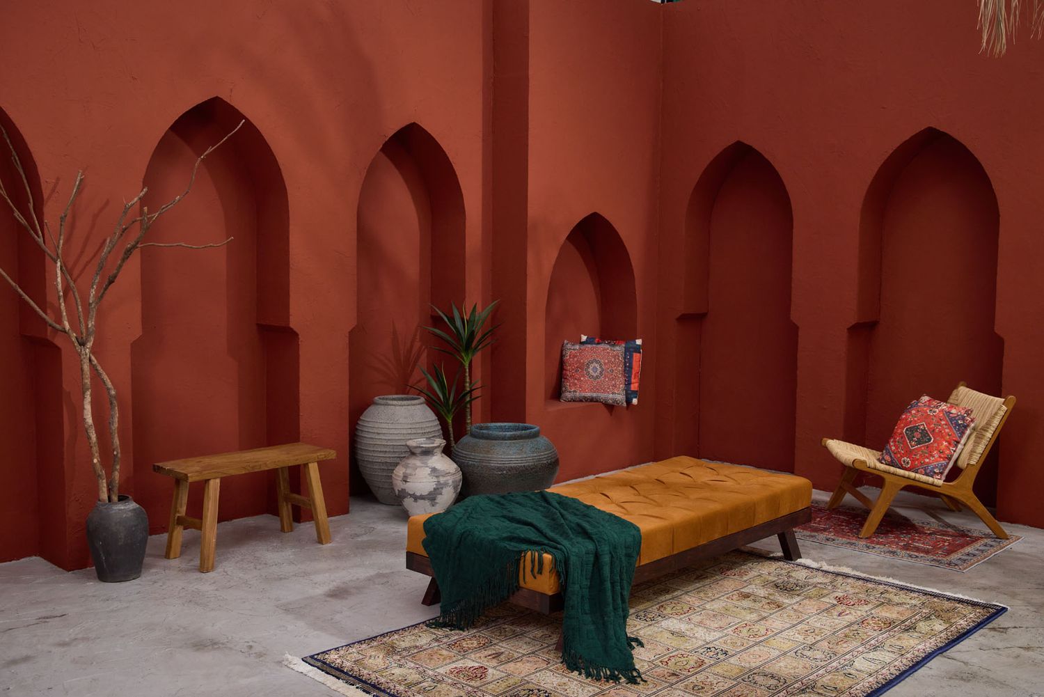 Moroccan-inspired terracotta courtyard with arched niches, vintage rugs, ochre daybed, and green throw blanket.