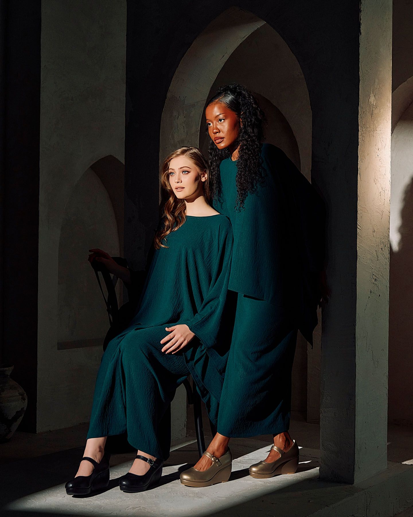 Two women in matching teal outfits posing in arched doorway wearing black and wedge shoes.