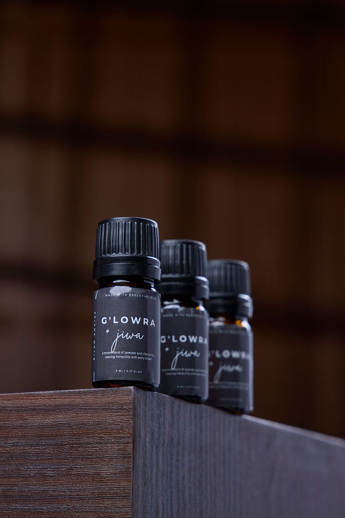 Four G'LOWRA Jiwa essential oil dark glass bottles lined up on a wooden shelf in moody dark setting.
