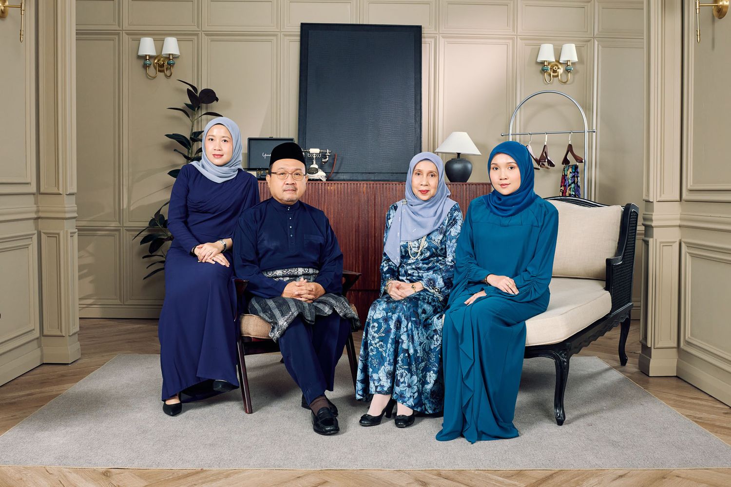 Malaysian family of four in elegant navy and blue traditional outfits seated for formal Eid portrait.