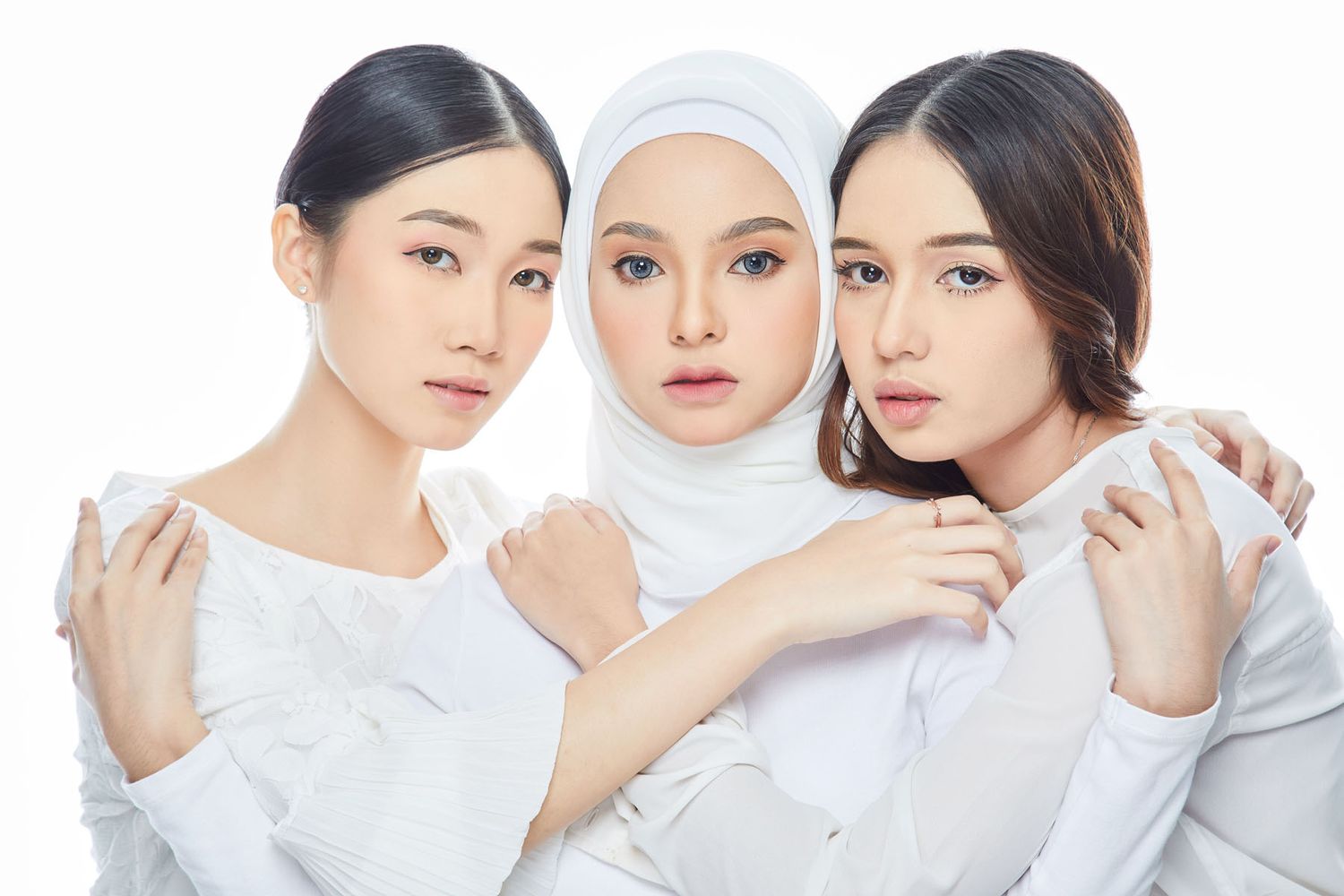 Three elegant women in white outfits posing together for a skincare beauty campaign photo shoot.