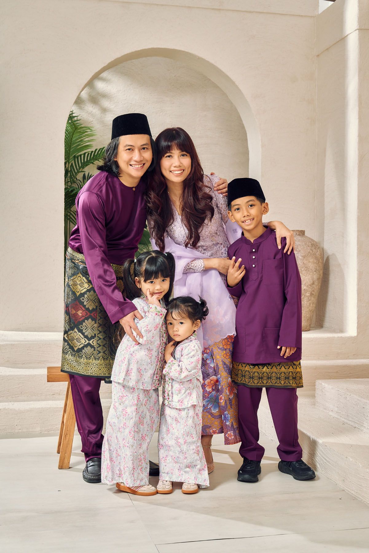 Happy Malaysian family in matching purple Baju Melayu and Baju Kurung outfits posing together.