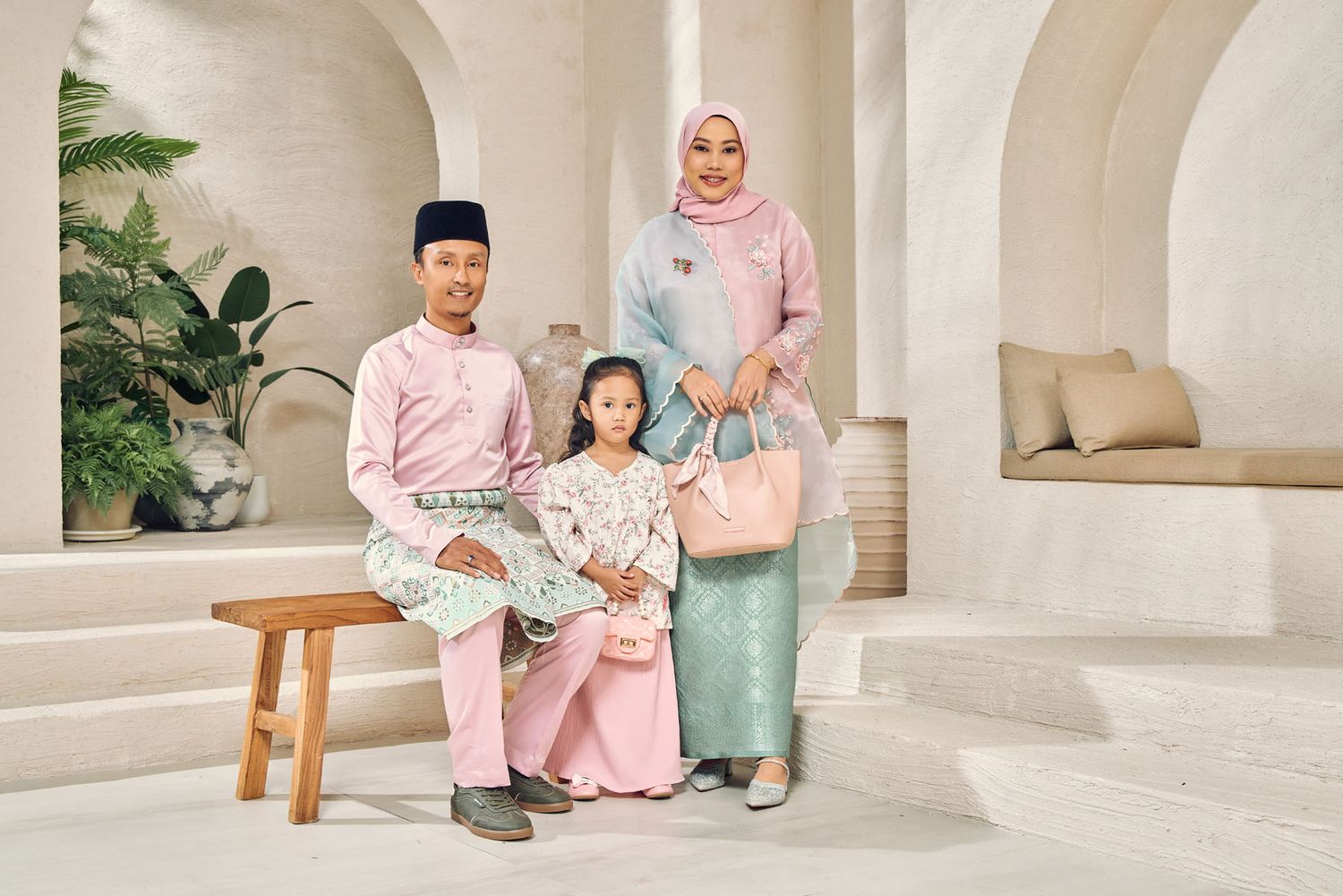 Malaysian couple with child wearing pastel pink and green traditional baju kurung and baju melayu Eid outfits.