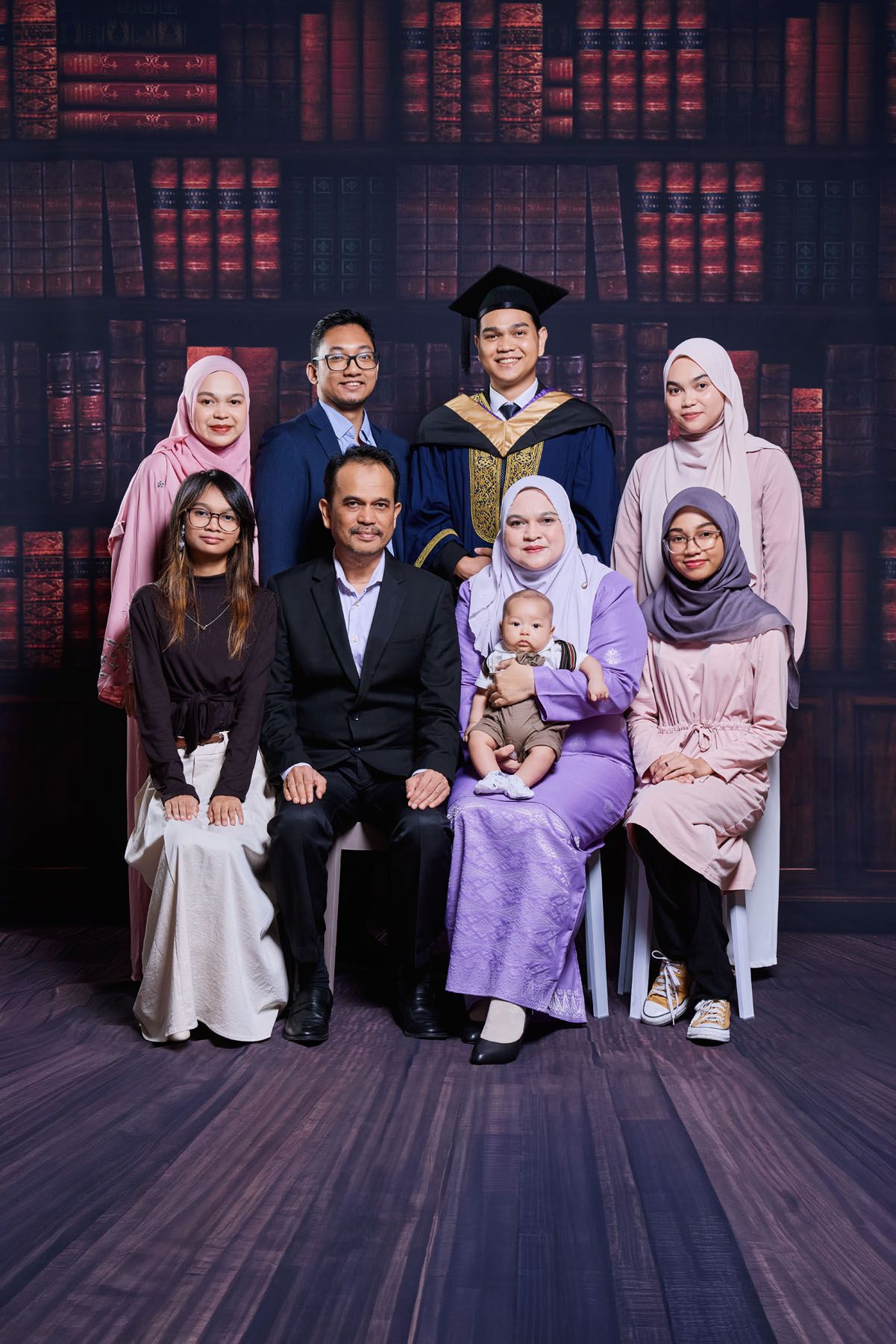 Large Malaysian family graduation portrait with graduate in blue robe surrounded by parents and siblings.