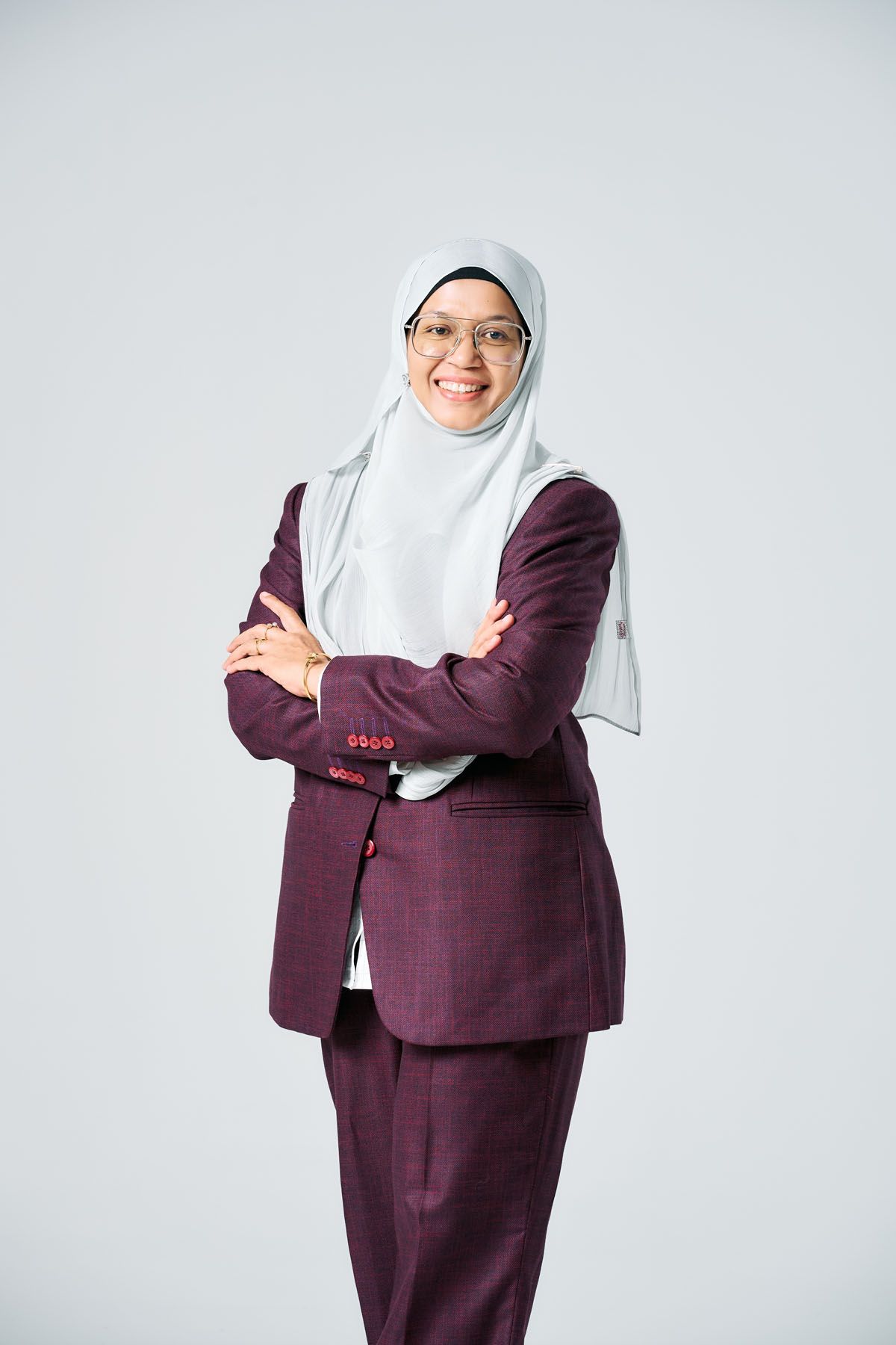 Professional Muslim businesswoman in hijab and maroon suit standing with arms crossed, smiling confidently.