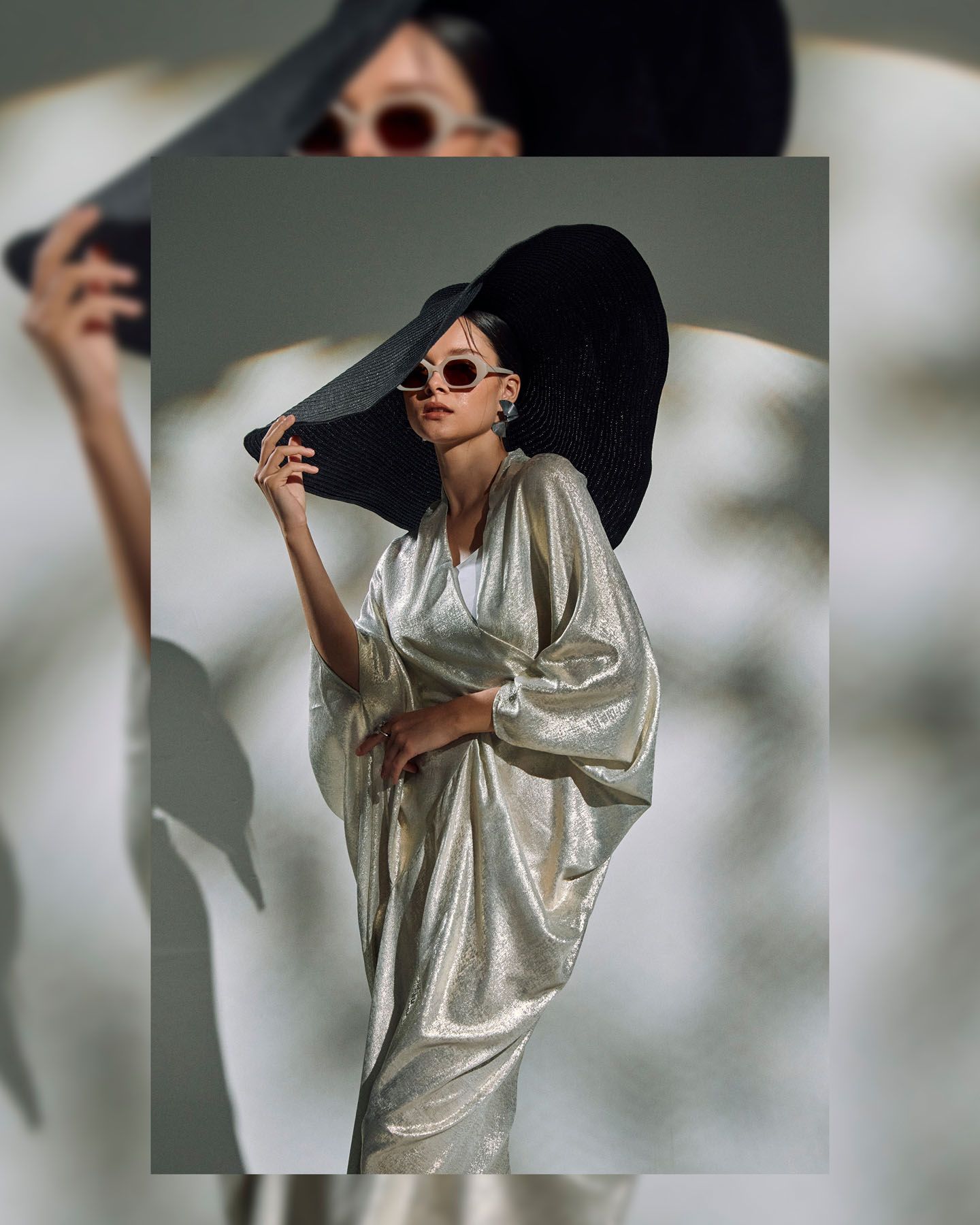 Woman in gold metallic kaftan dress wearing a wide-brim black hat and retro sunglasses in editorial shot.
