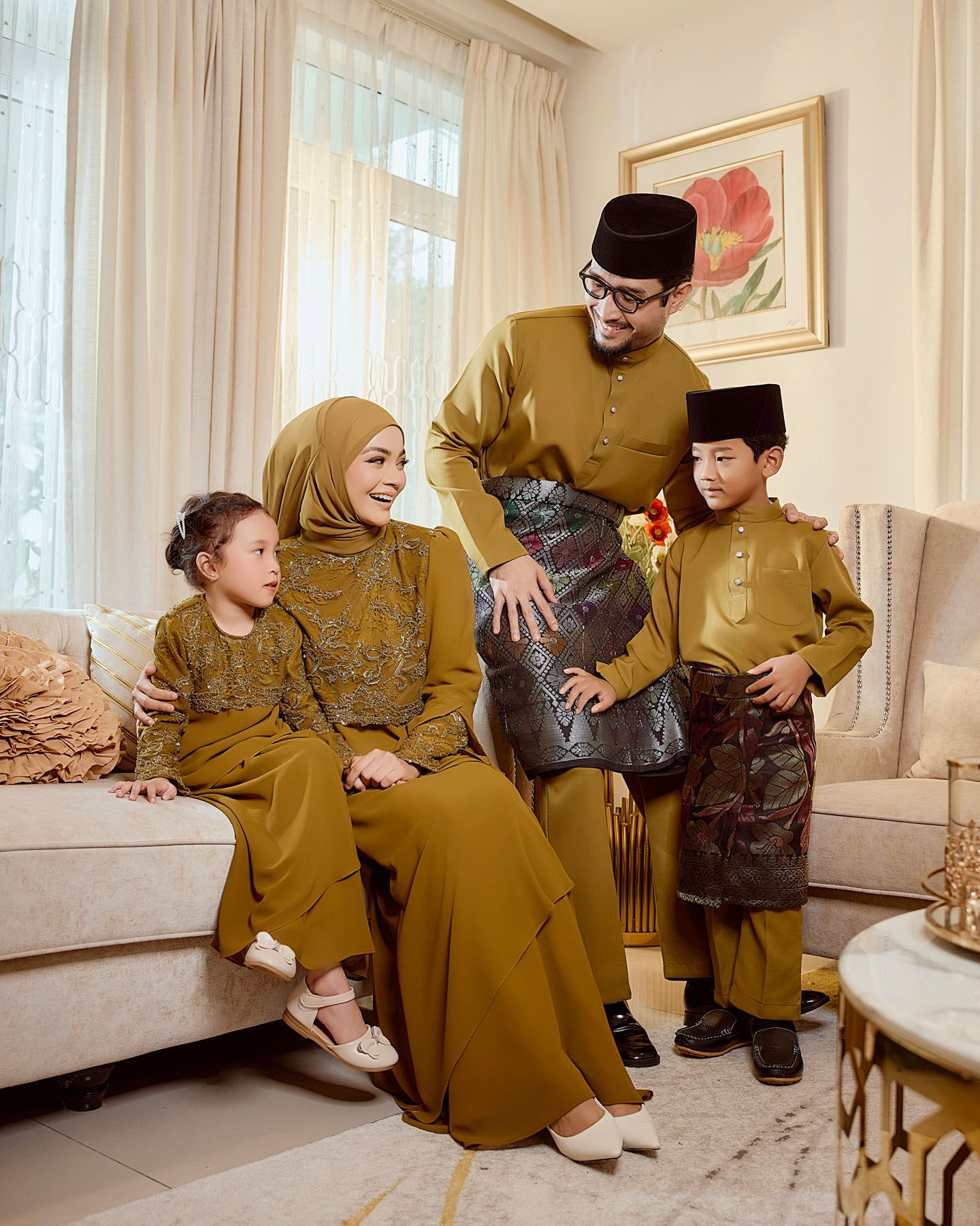 Family of four in matching mustard gold traditional Malaysian outfits posing in a cozy living room.
