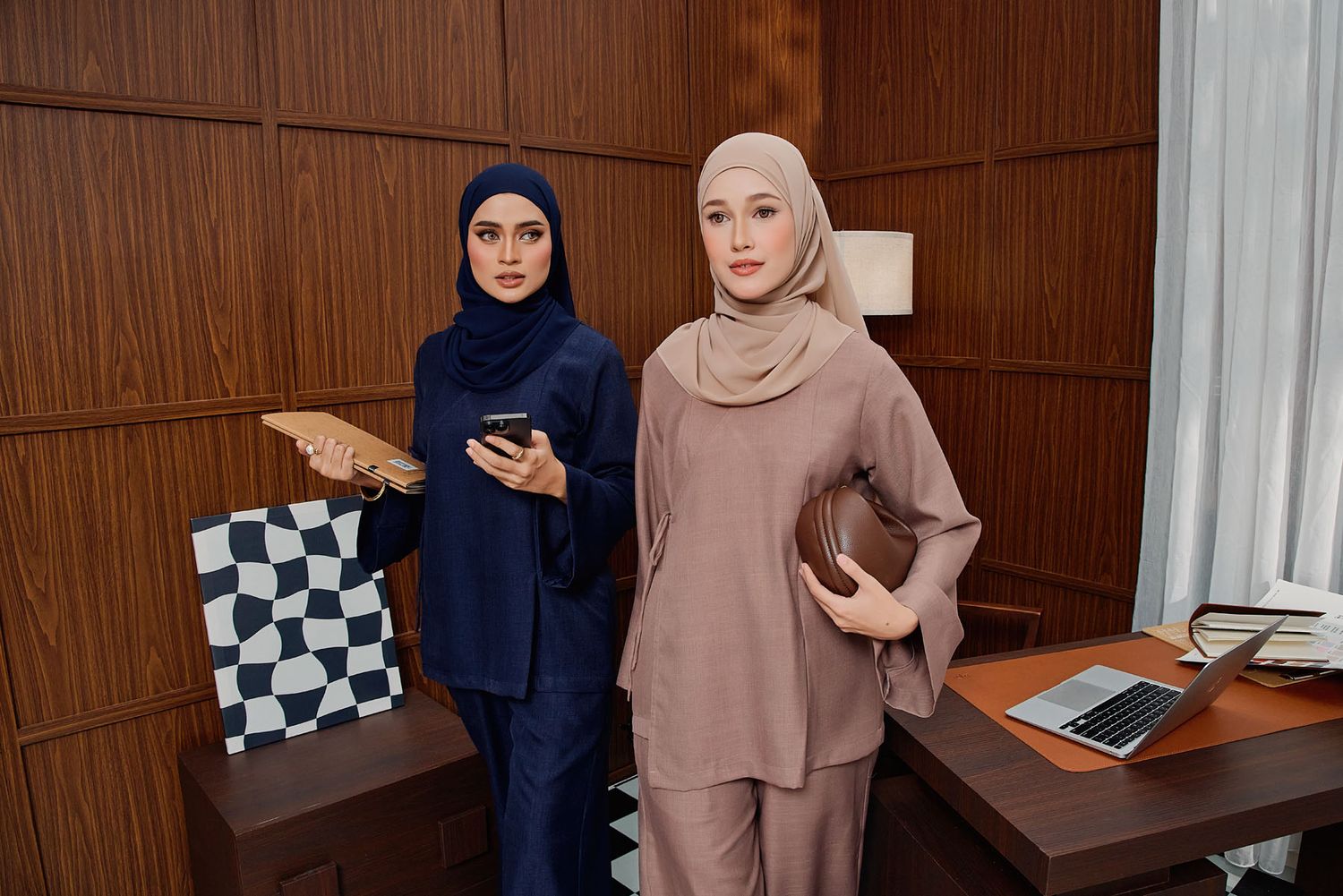 Two Muslim women in navy and beige modest hijab outfits in modern office.