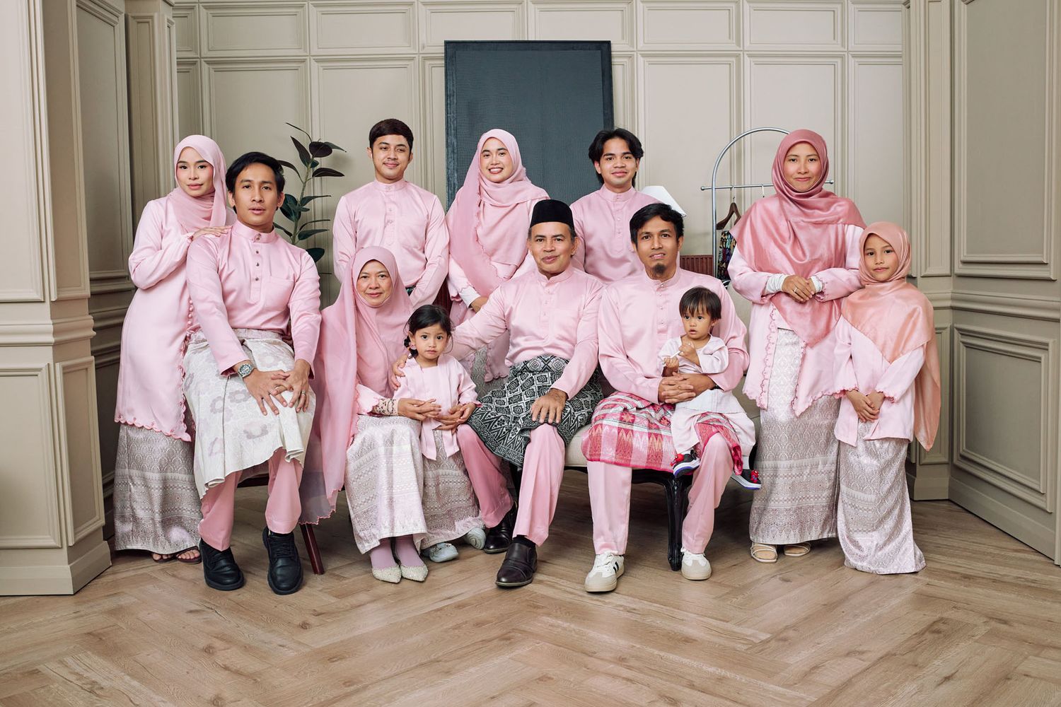 Extended Muslim family dressed in matching pink baju raya traditional attire posing for a formal Hari Raya family portrait.
