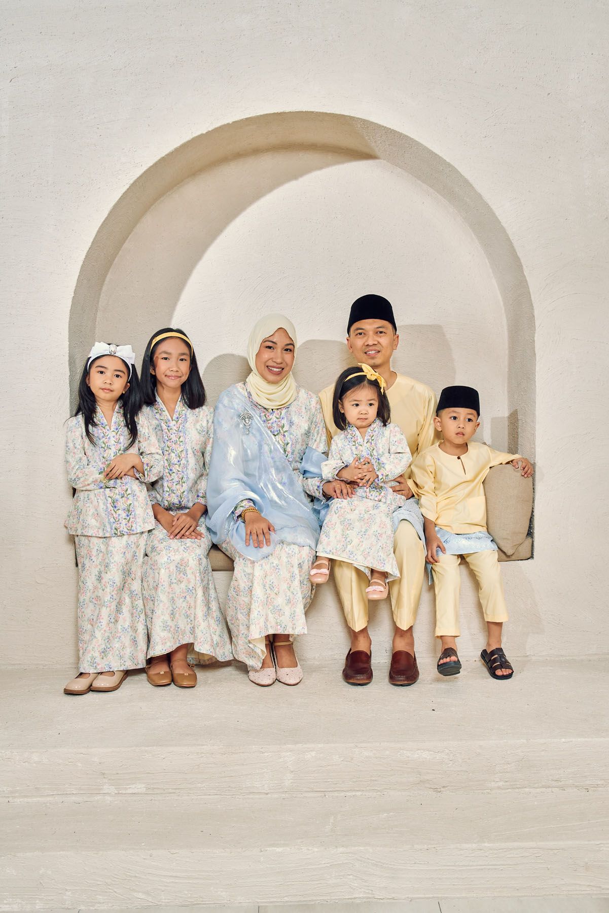 Muslim family of six in blue and gold traditional Eid attire seated under white arch.
