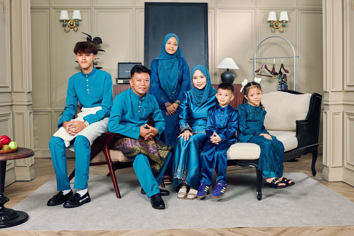 Malaysian family of five in matching teal Baju Melayu and Baju Kurung sitting in elegant room.