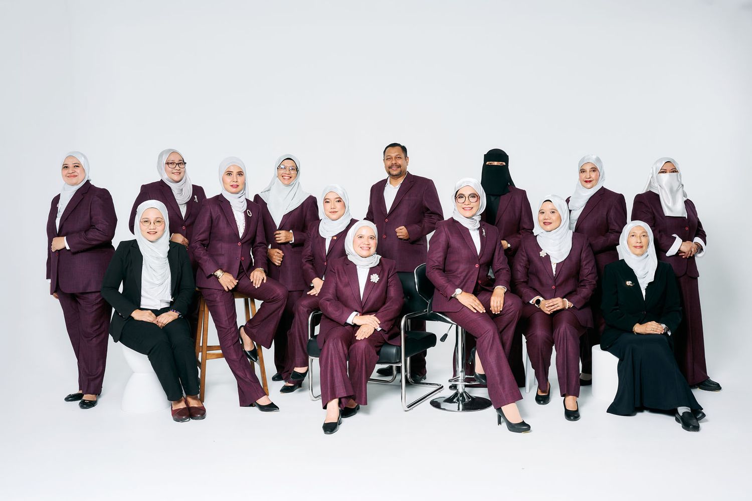 Group of women in matching burgundy suits and white hijabs posing together for a professional photo shoot.
