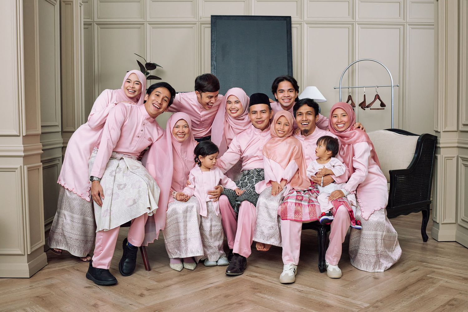 Happy Muslim family group wearing coordinated pink traditional Malay baju raya outfits smiling together for Eid portrait.