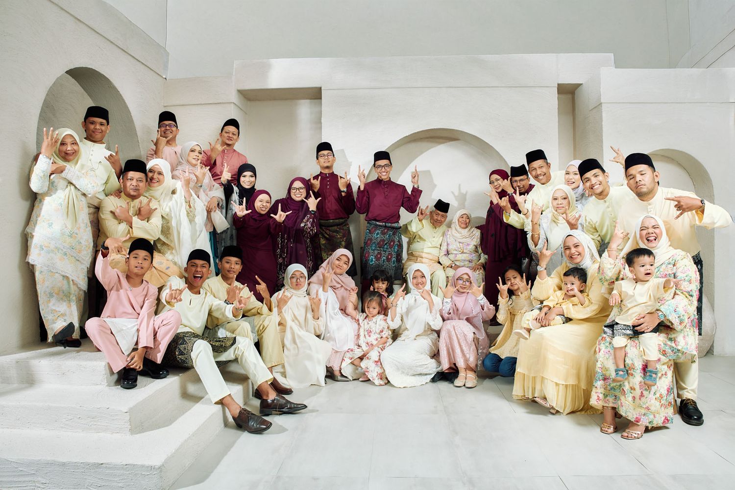 Extended Malaysian family posing together in coordinated traditional Eid festive clothing indoors.