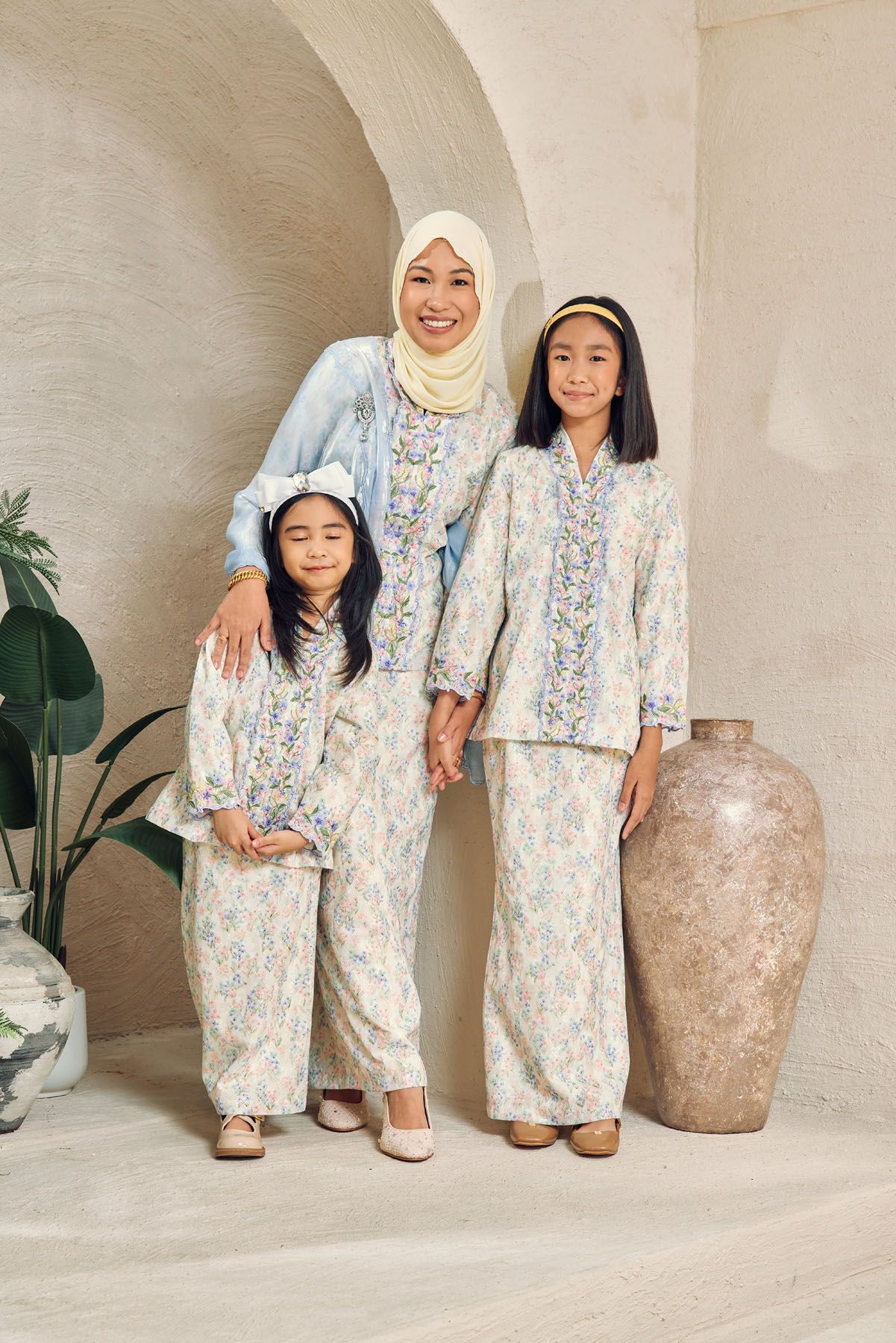 Muslim mother in hijab with two daughters wearing matching floral baju kurung outfits.