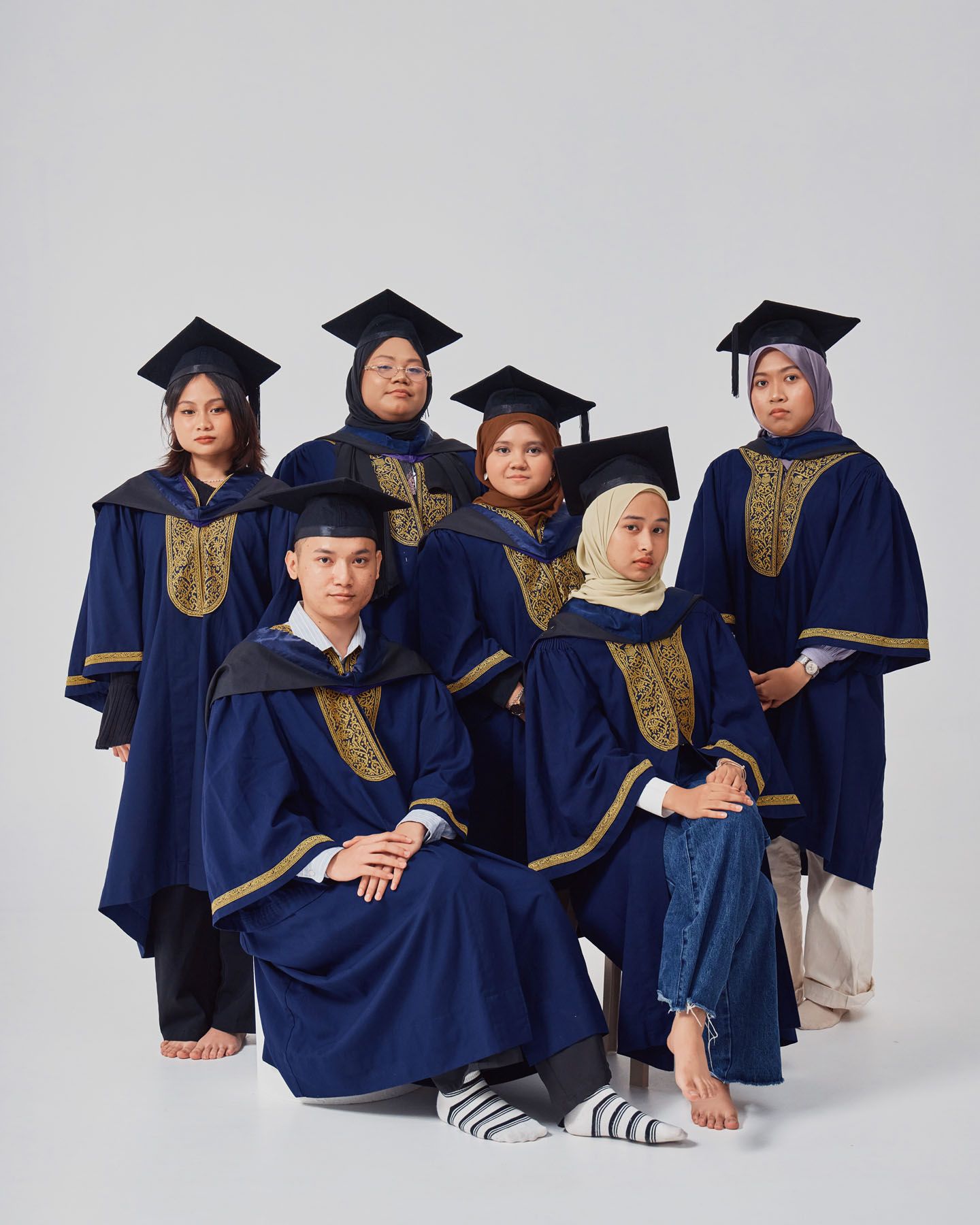 Seven graduates in navy and gold academic robes posing together for a formal graduation portrait.
