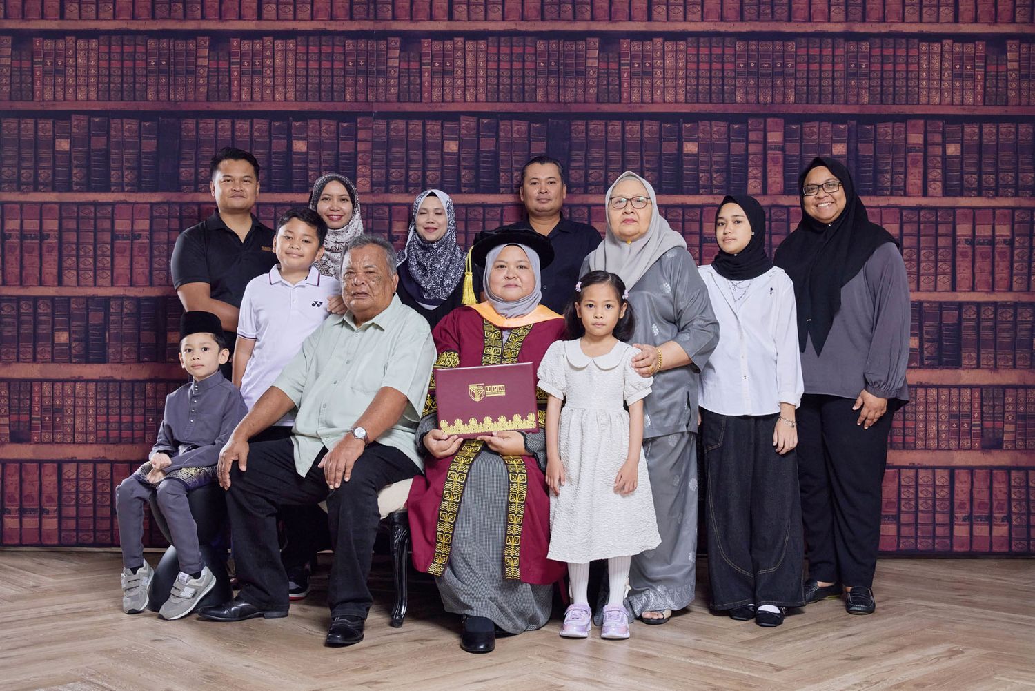 Large Muslim family group portrait posing in front of decorative bookshelf background.