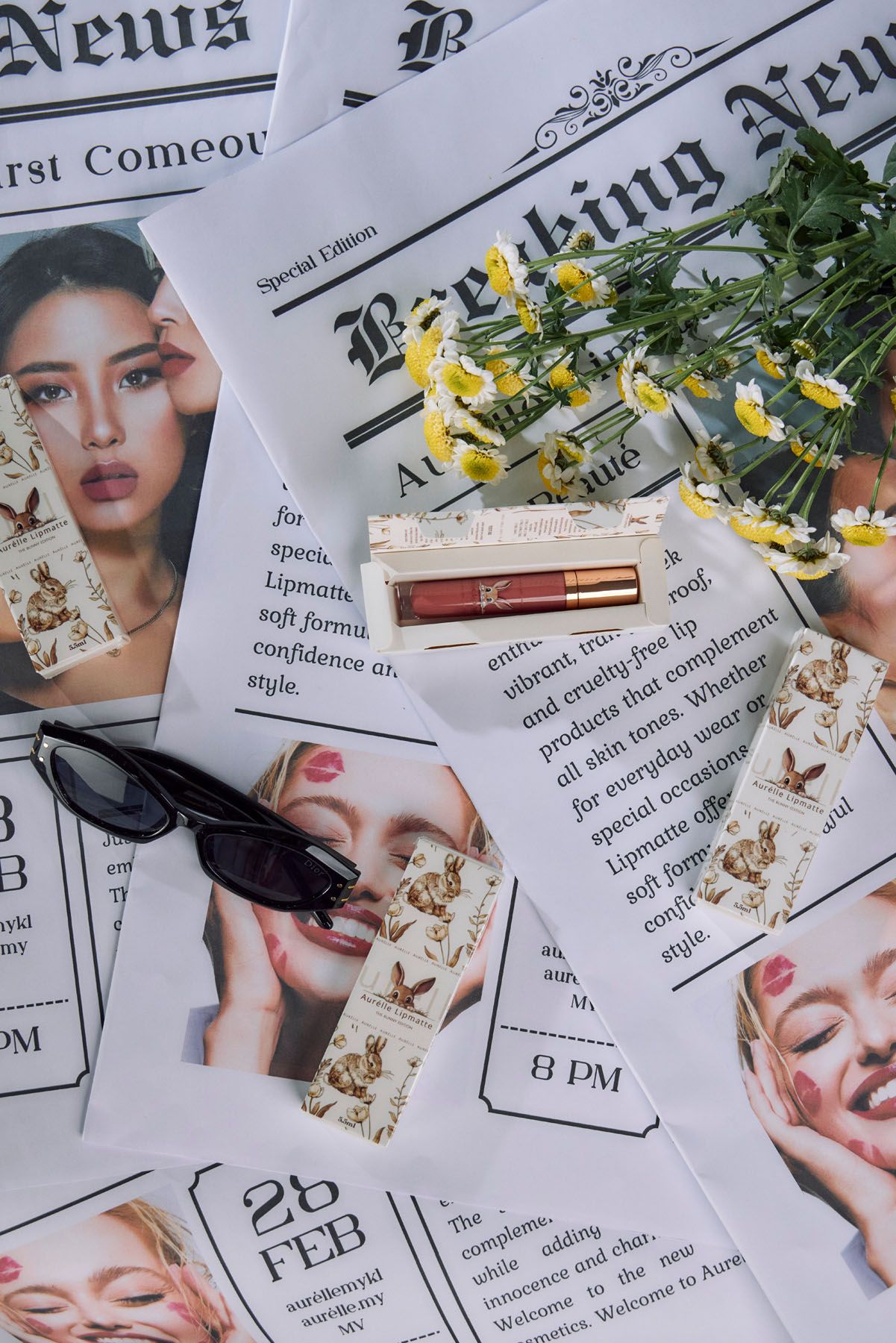 Aurelle lip matte products displayed on newspaper pages with sunglasses, flowers, and model photos in flat lay.