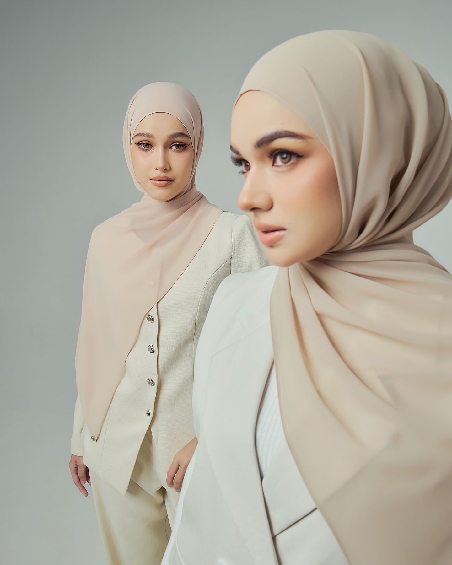Two women wearing beige hijabs and cream blazer outfits posing together in a professional fashion shoot.