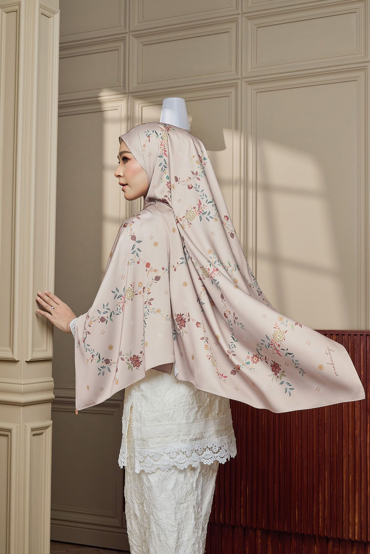 Back view of woman wearing floral pink hijab and white lace baju kurung in a stylish interior.