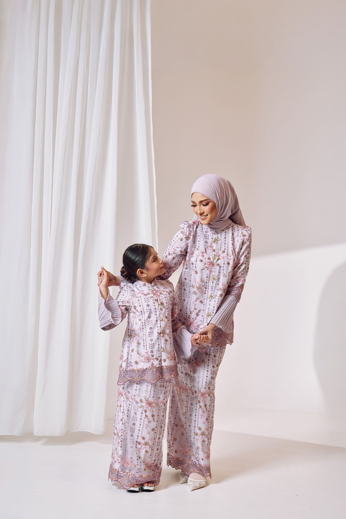 Muslim mother and daughter wearing matching floral printed baju kurung sets in a soft white studio setting.