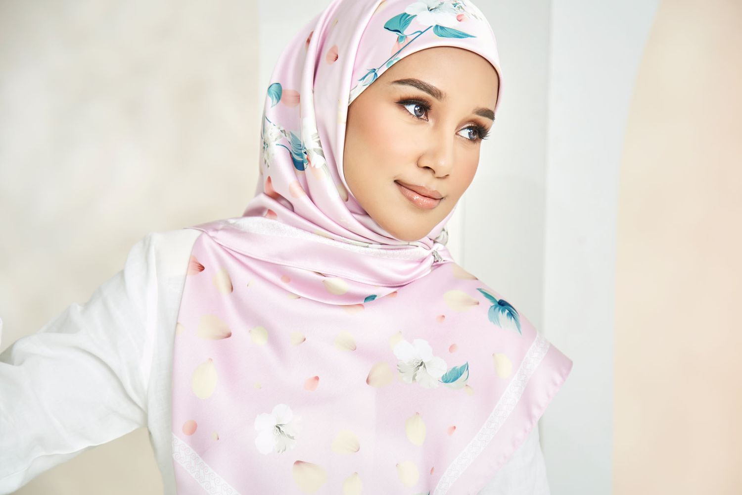 Beautiful Muslim woman wearing a light pink floral printed hijab in a soft natural setting.