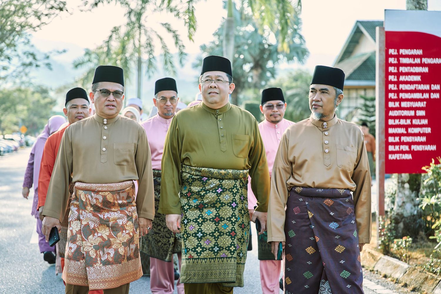 Malaysian men in traditional Baju Melayu with songket sarongs walking formally at an official outdoor ceremony.