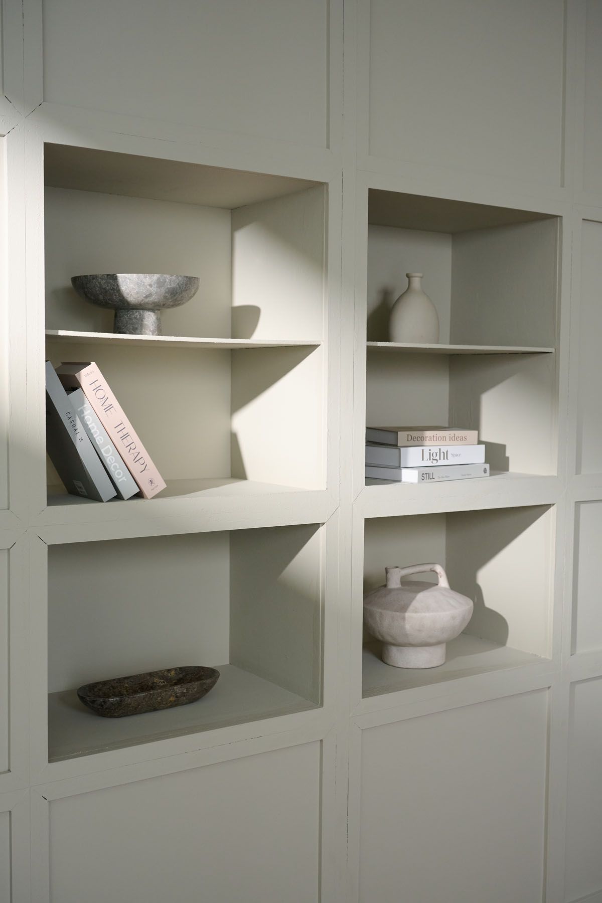 Elegant built-in shelving unit painted sage green displaying ceramic vases, decorative bowls, and curated books.