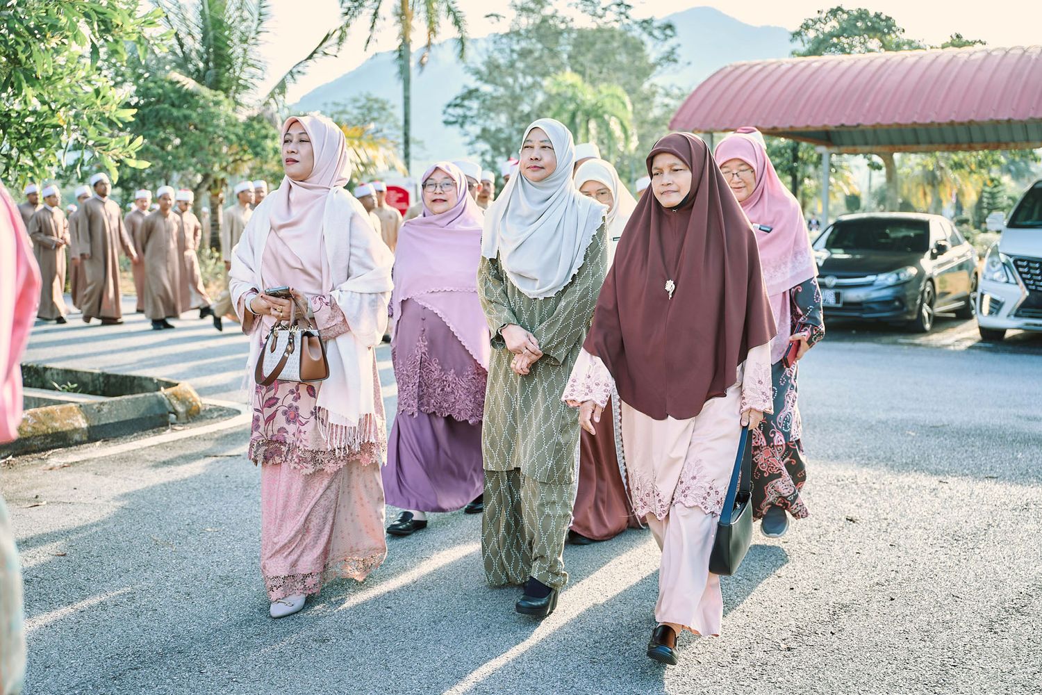 Group of Muslim women in hijabs and colorful baju kurung walking together at an outdoor cultural event.